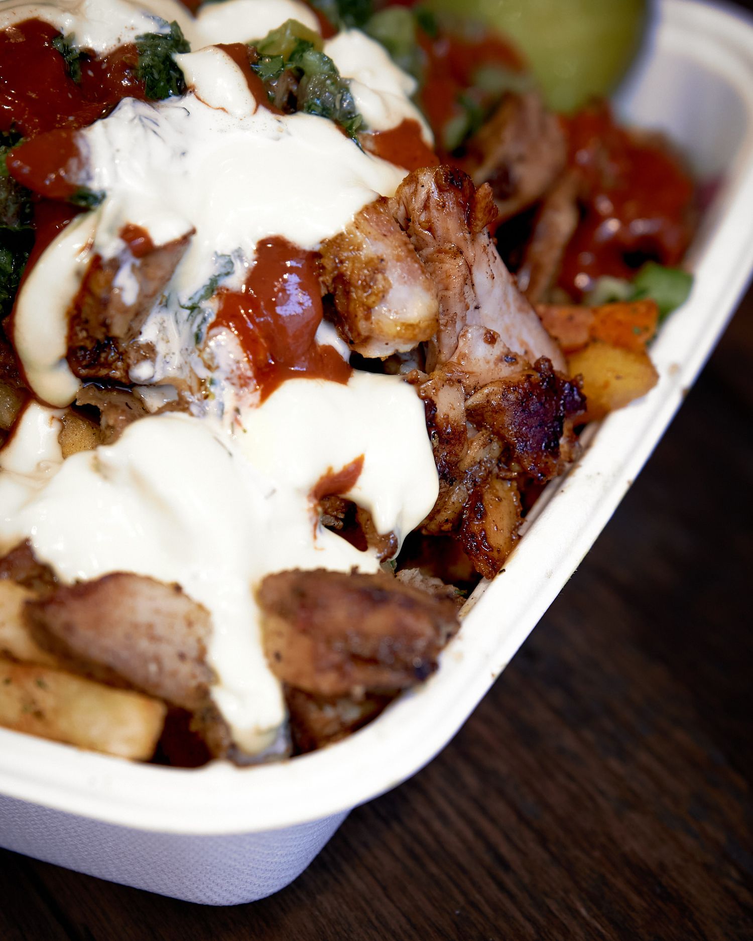 Grilled meat dish topped with creamy white sauce and fresh herbs in white serving bowl.