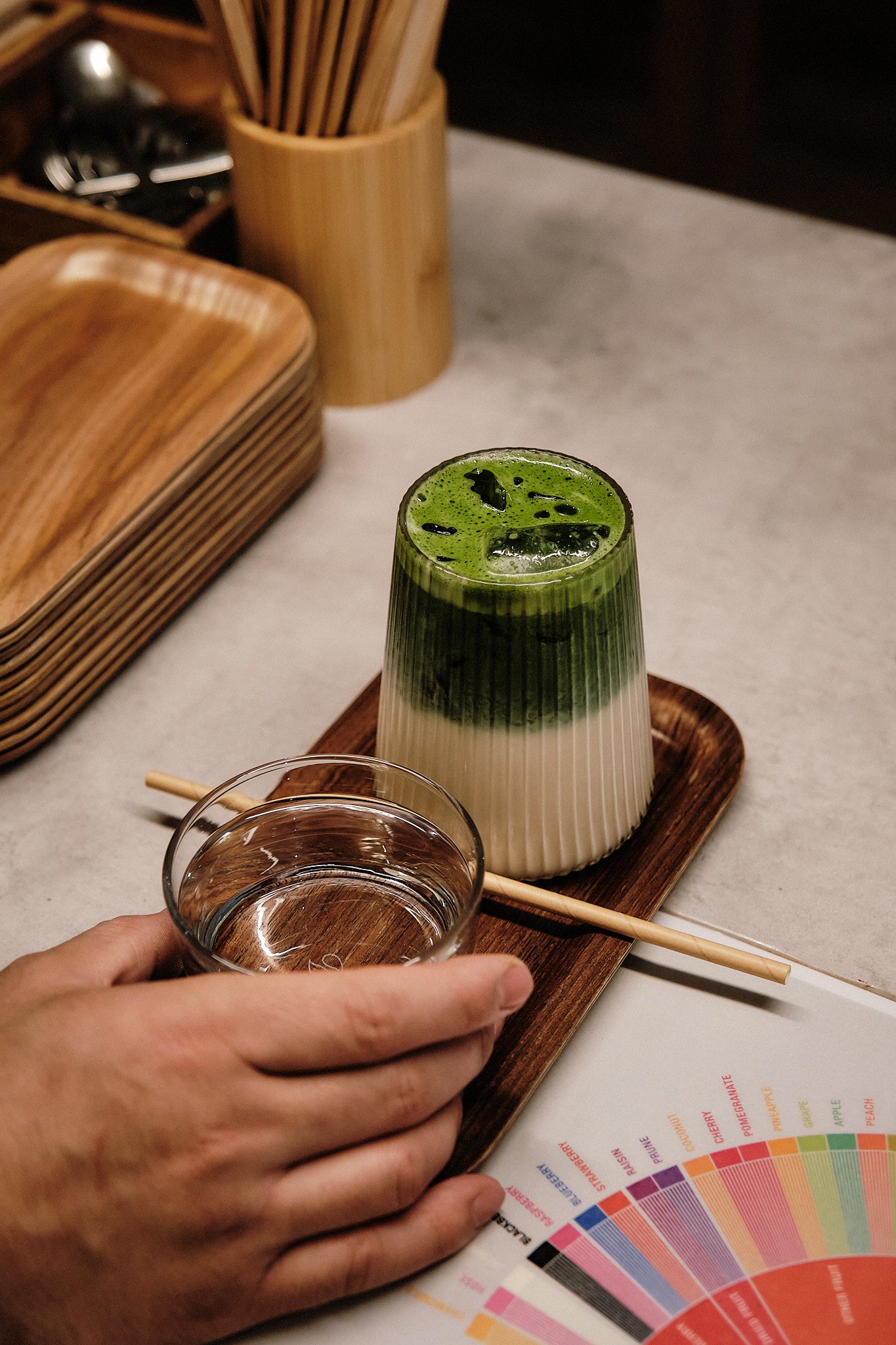 A green matcha tea drink served in a glass with a wooden serving board and color chart.