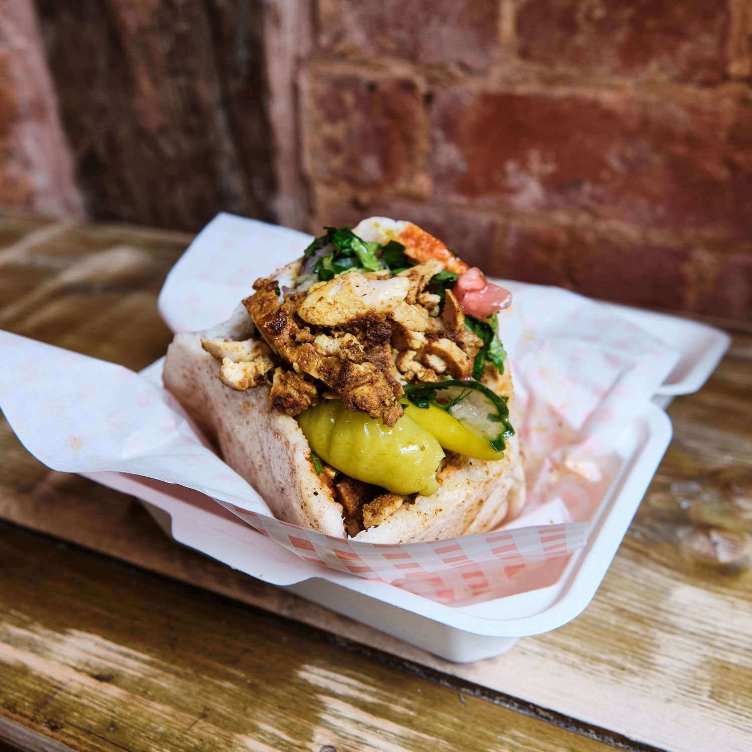 Artisanal sandwich with fresh toppings displayed on white paper against rustic background.