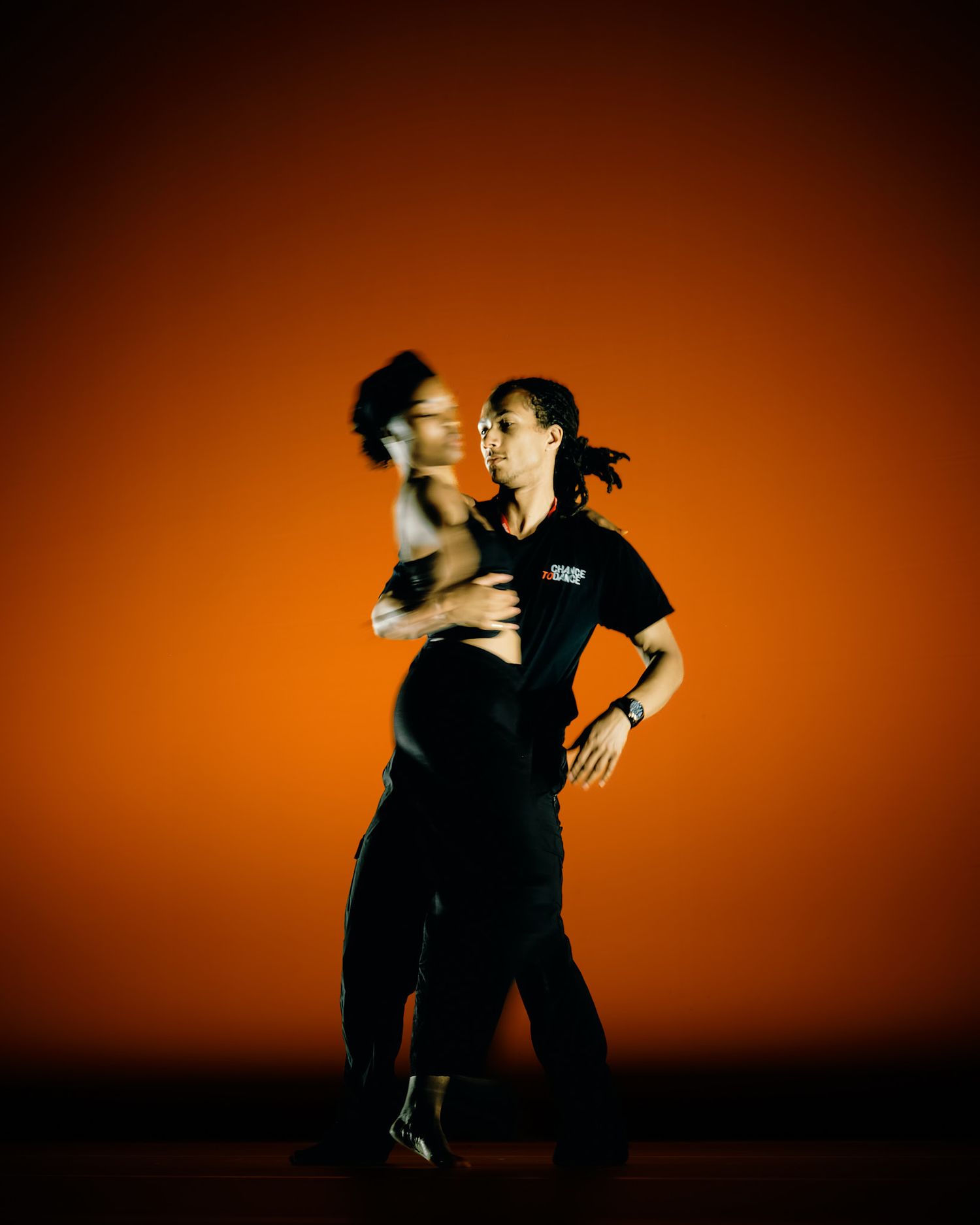 Two silhouetted figures dance expressively against a dramatic orange sunset backdrop in a sequence of artistic movements.