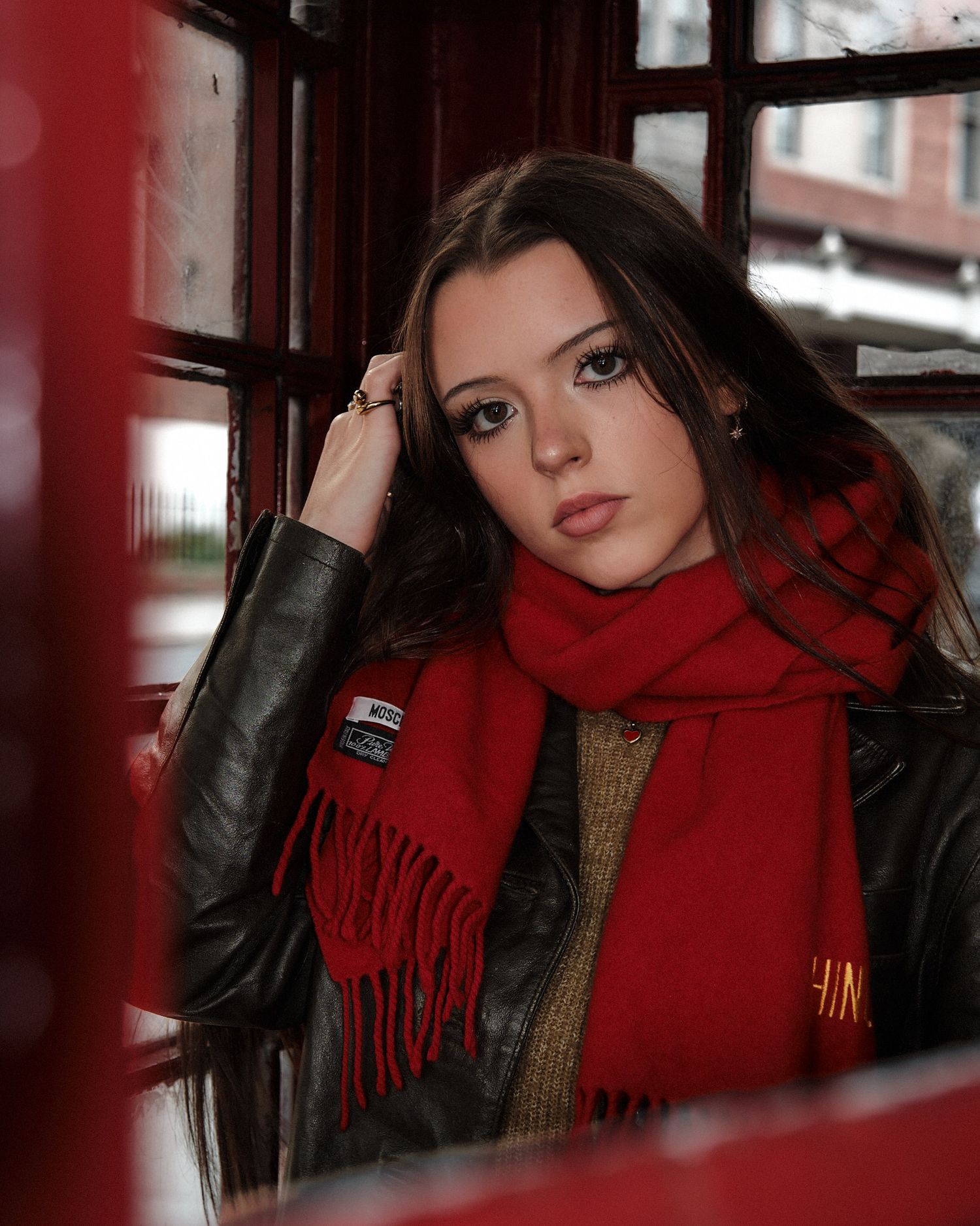 Fashion portrait in red phone booth featuring dark leather jacket and bright red scarf styled with moody lighting.