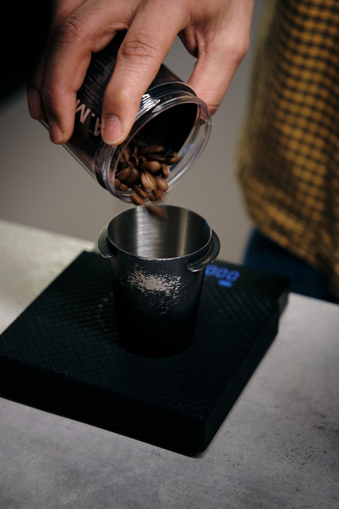 Hands tamping coffee grounds into a portafilter on a dark counter surface.