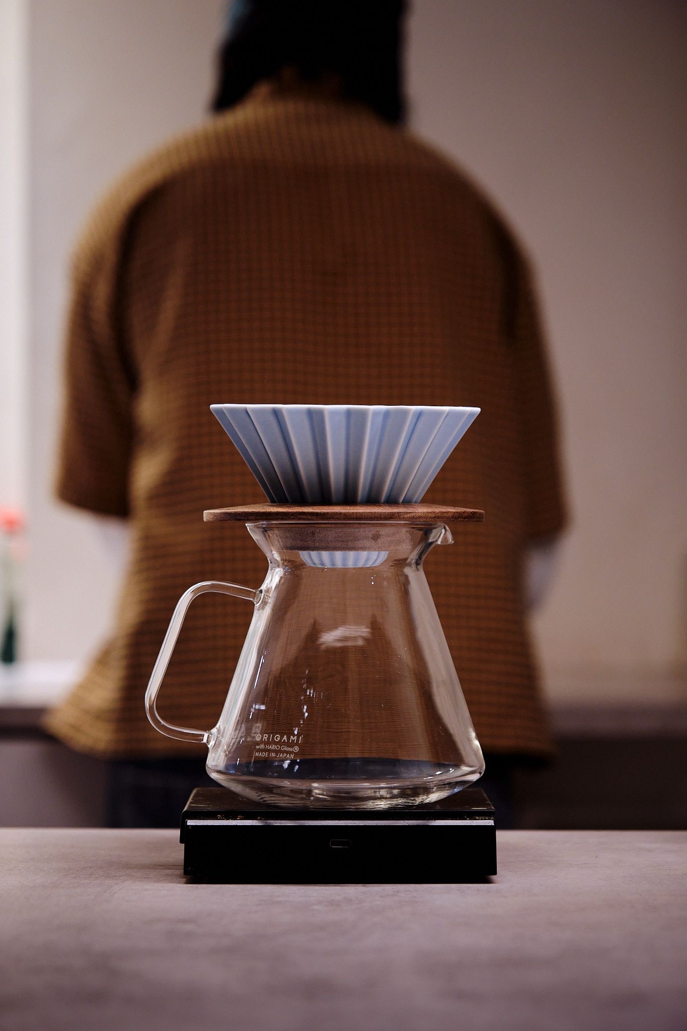 A minimalist coffee brewing station featuring a glass Hario V60 dripper and blue paper filter.