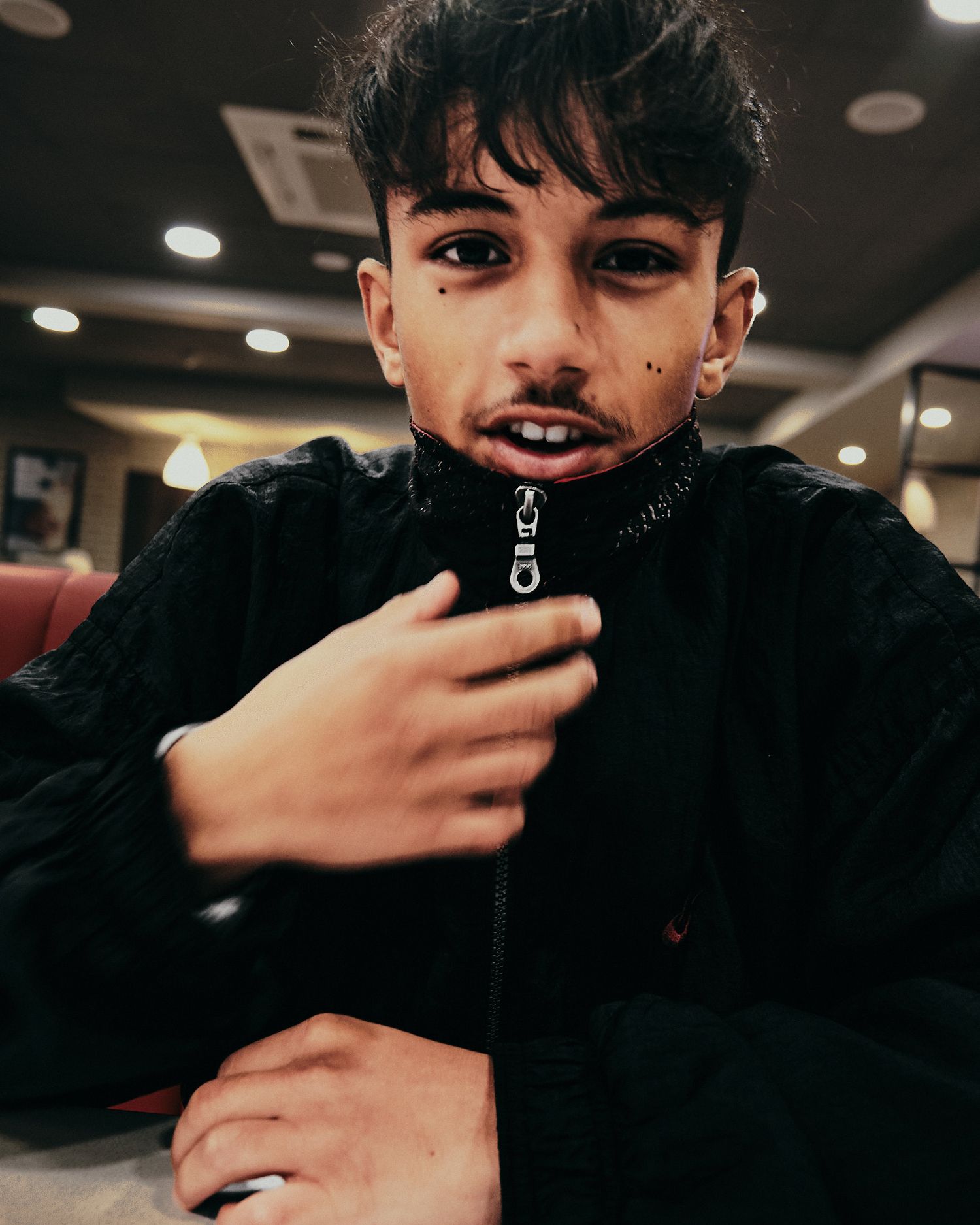 Candid fashion portrait showing black zip-up jacket in dim indoor lighting.