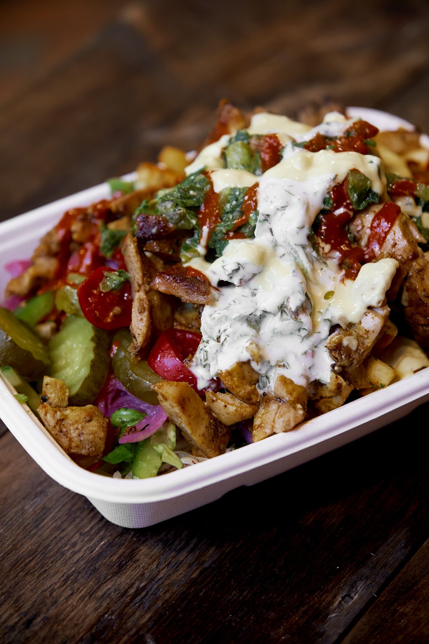 Mediterranean-style loaded fries topped with tzatziki sauce and colorful vegetables in a white serving dish.