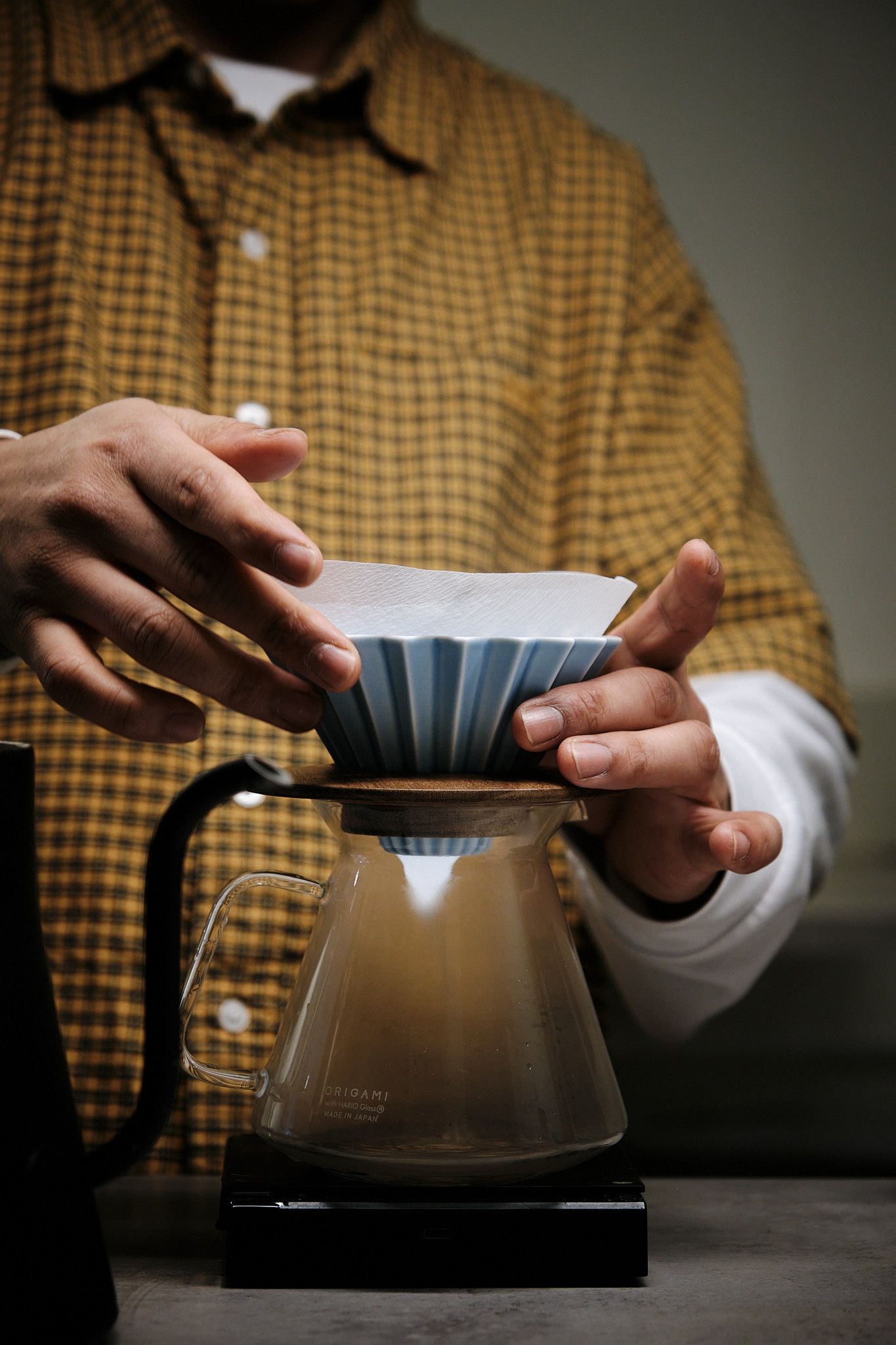 Hands carefully placing a blue filter paper into a glass Hario V60 coffee dripper.