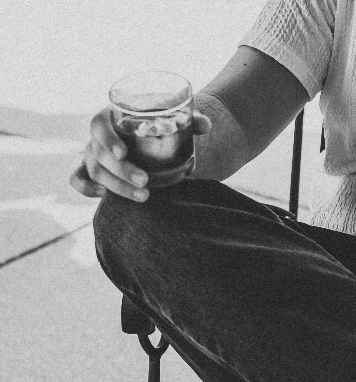 Person holding drink while relaxing in casual black attire.