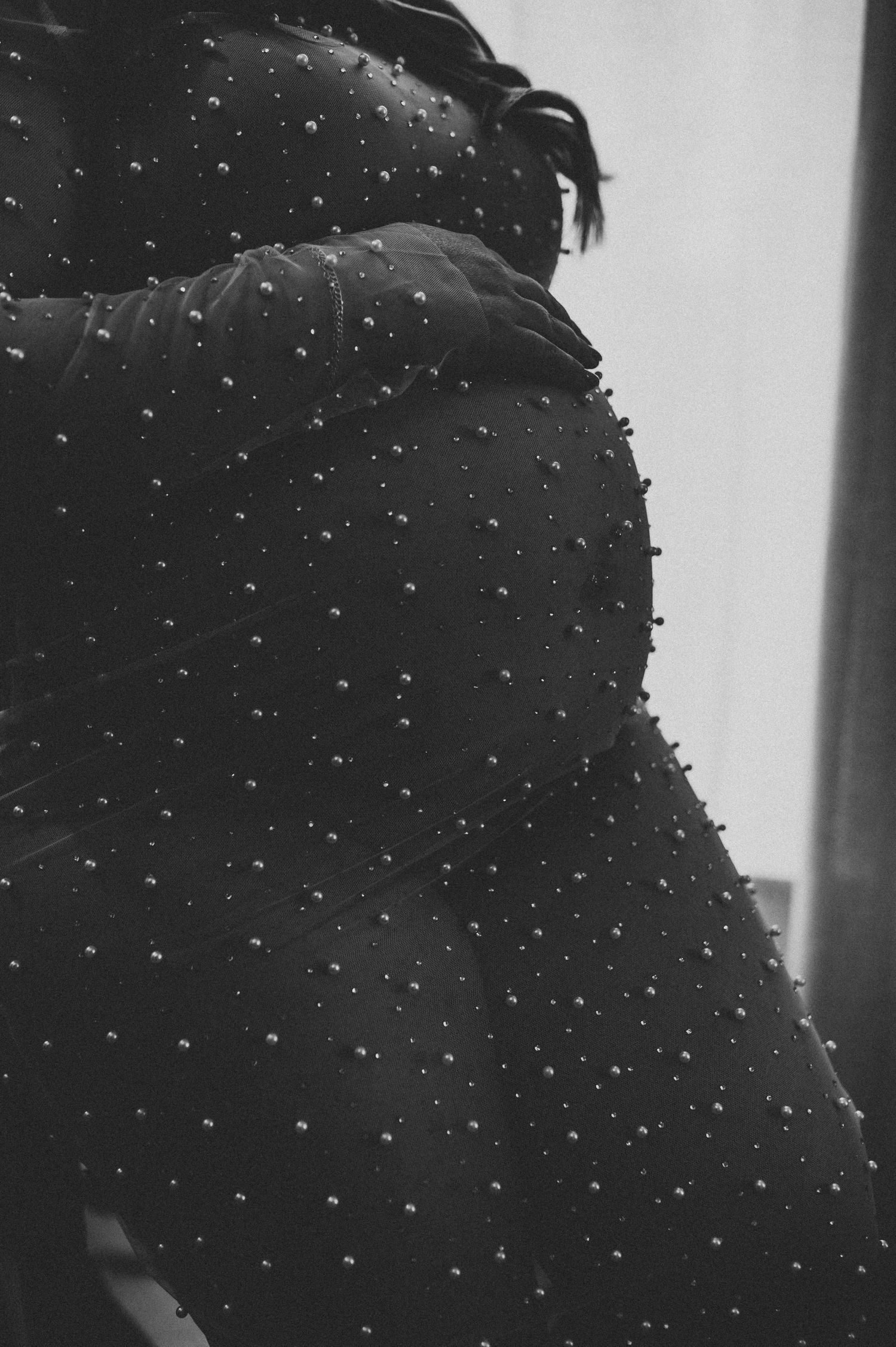 Black and white close-up of a studded black fabric garment with pearl embellishments on a figure.