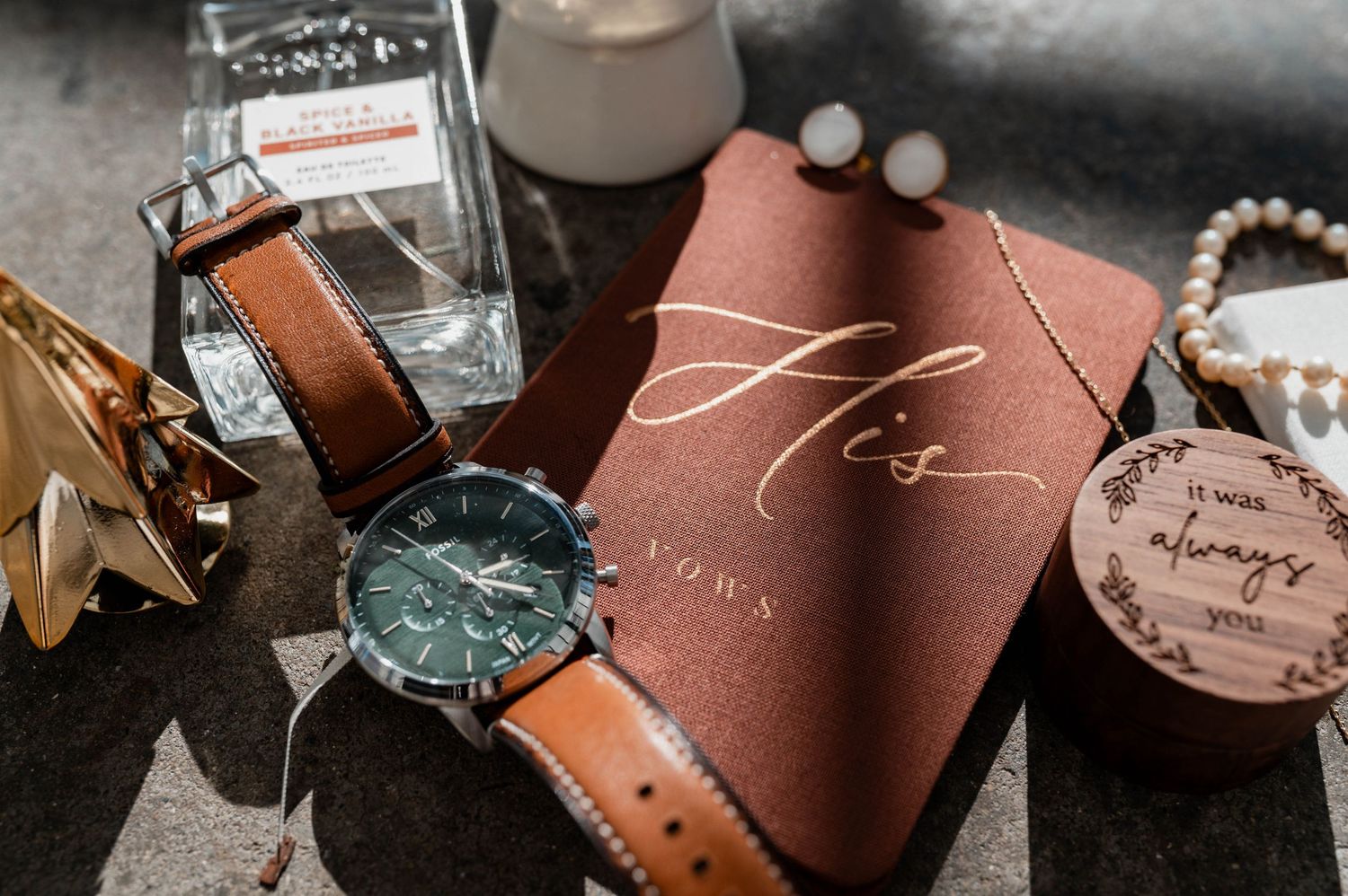 Groom's wedding flat lay with a VOWN watch, brown leather strap, cologne, pearl bracelet, and His vow book.
