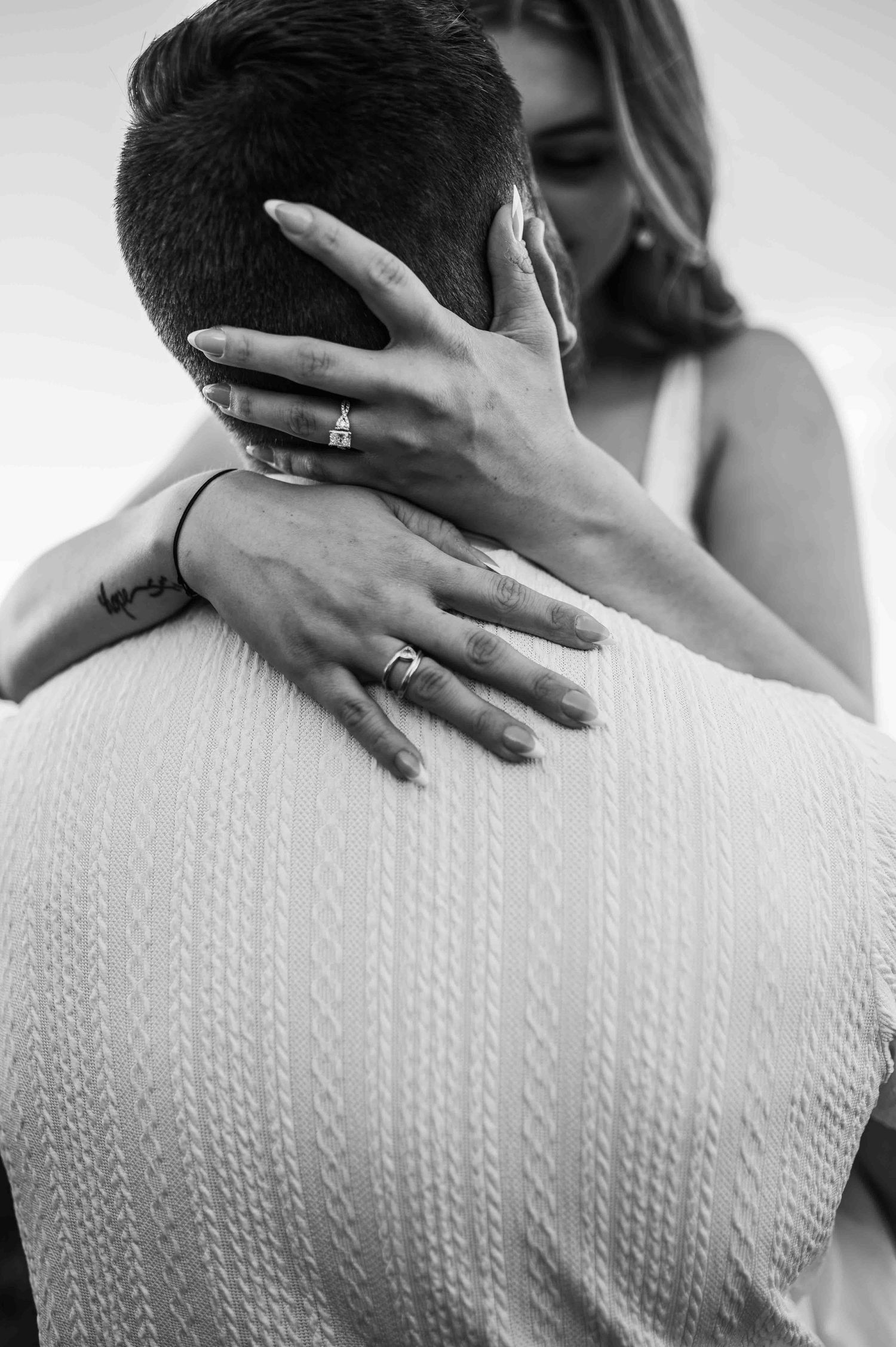 Black and white close-up of hands embracing against textured fabric.