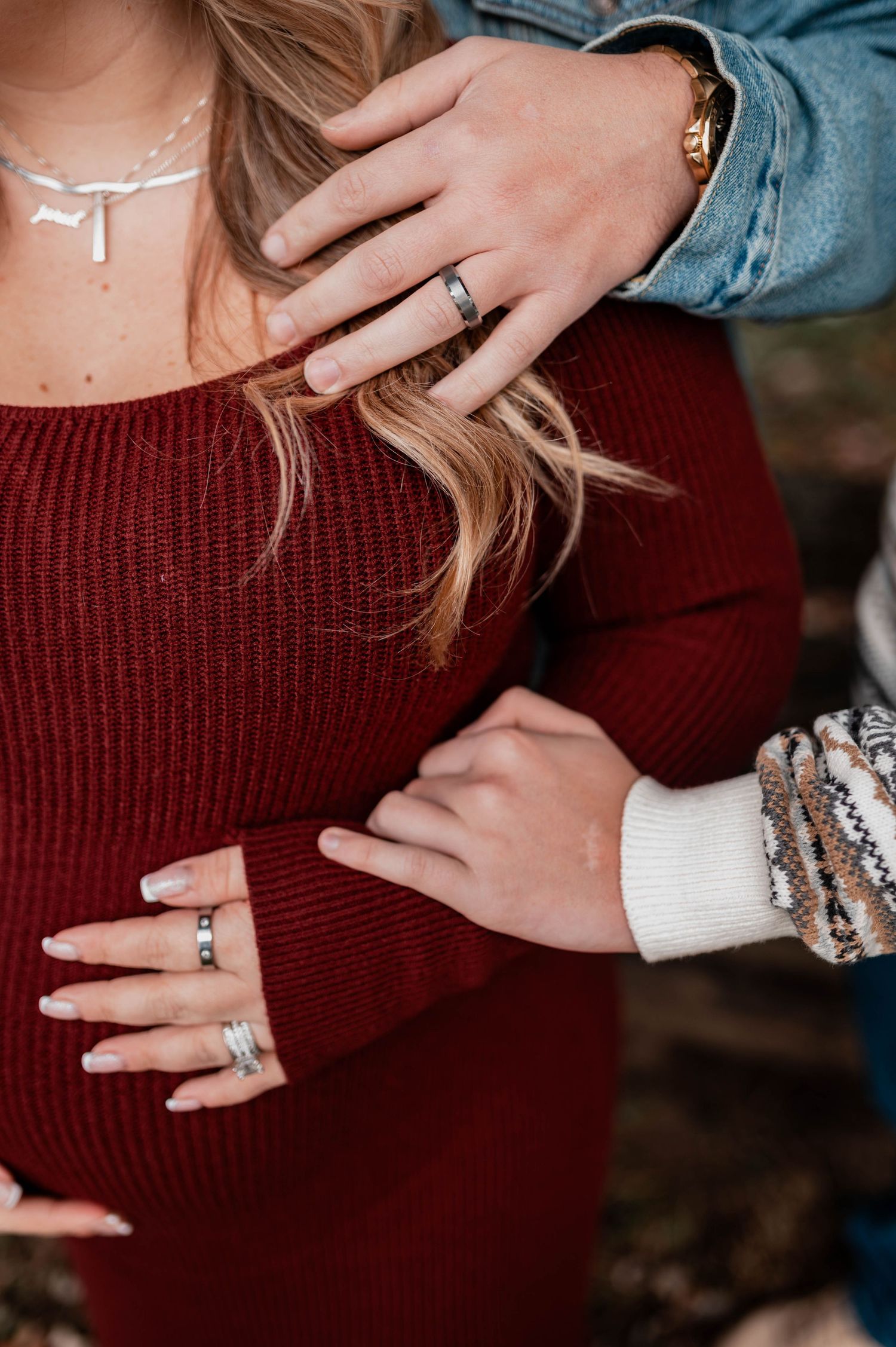 Close-up of couple embracing, showing wedding rings, bracelets, and a burgundy knit dress with a silver necklace.
