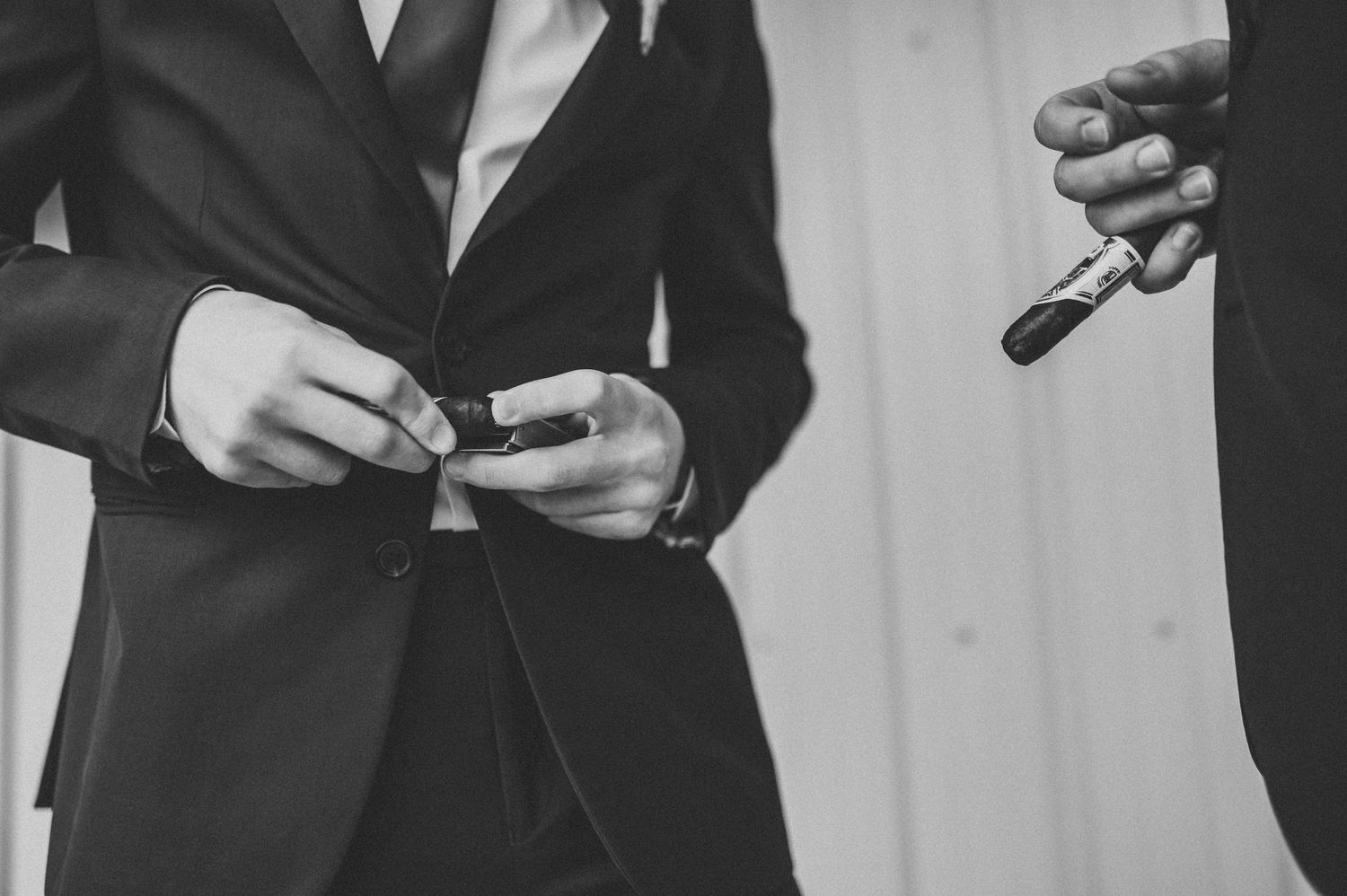 Black and white photo of two men in suits, one buttoning jacket while other holds a cigar.