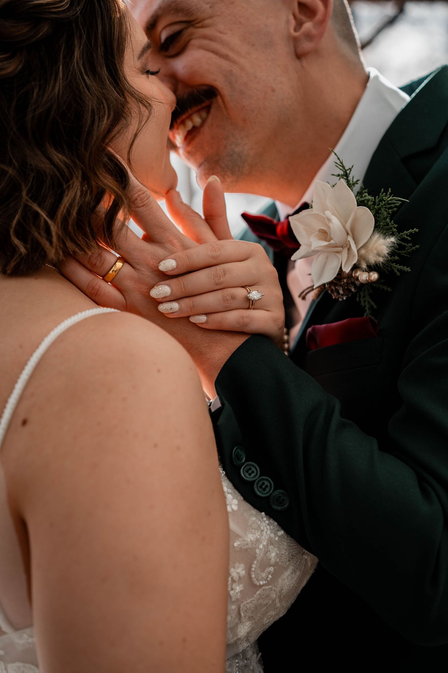 Bride and groom laughing together, showcasing wedding rings, with groom wearing a green suit and floral boutonniere.
