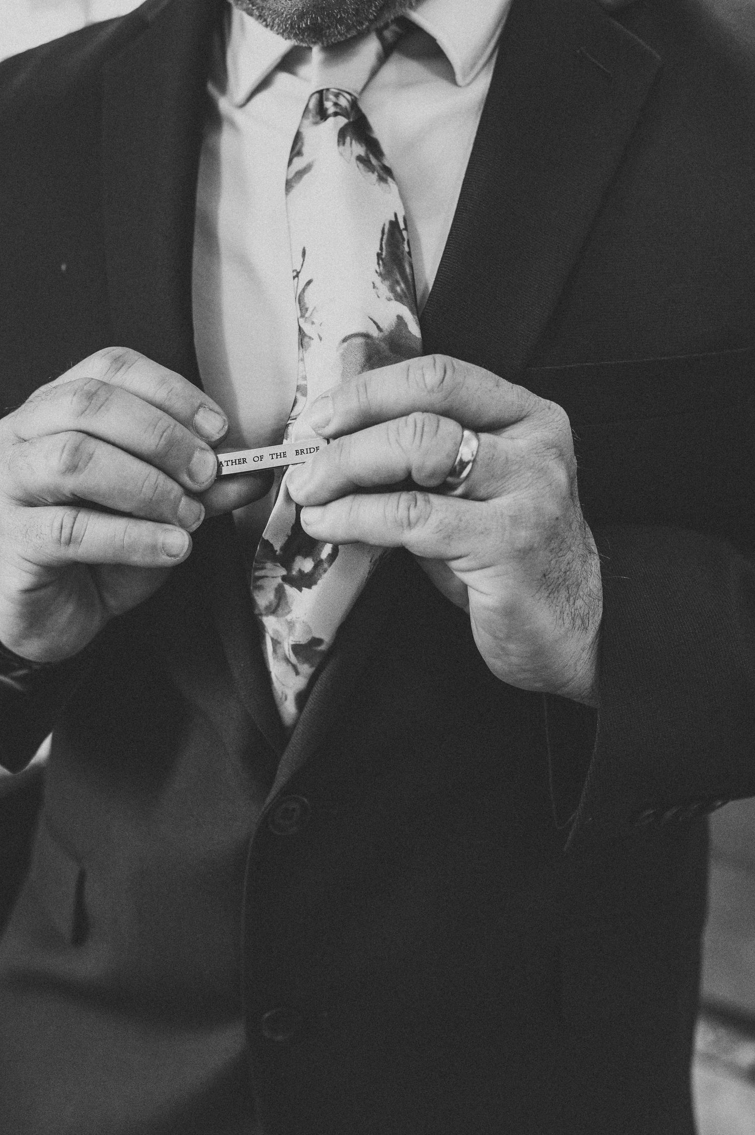 Close-up of hands adjusting a formal tie and suit jacket in black and white.