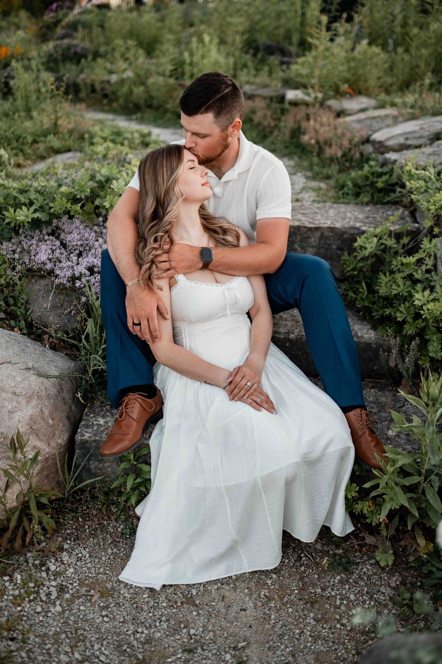 Couple in white dress and casual wear sitting together in garden setting.