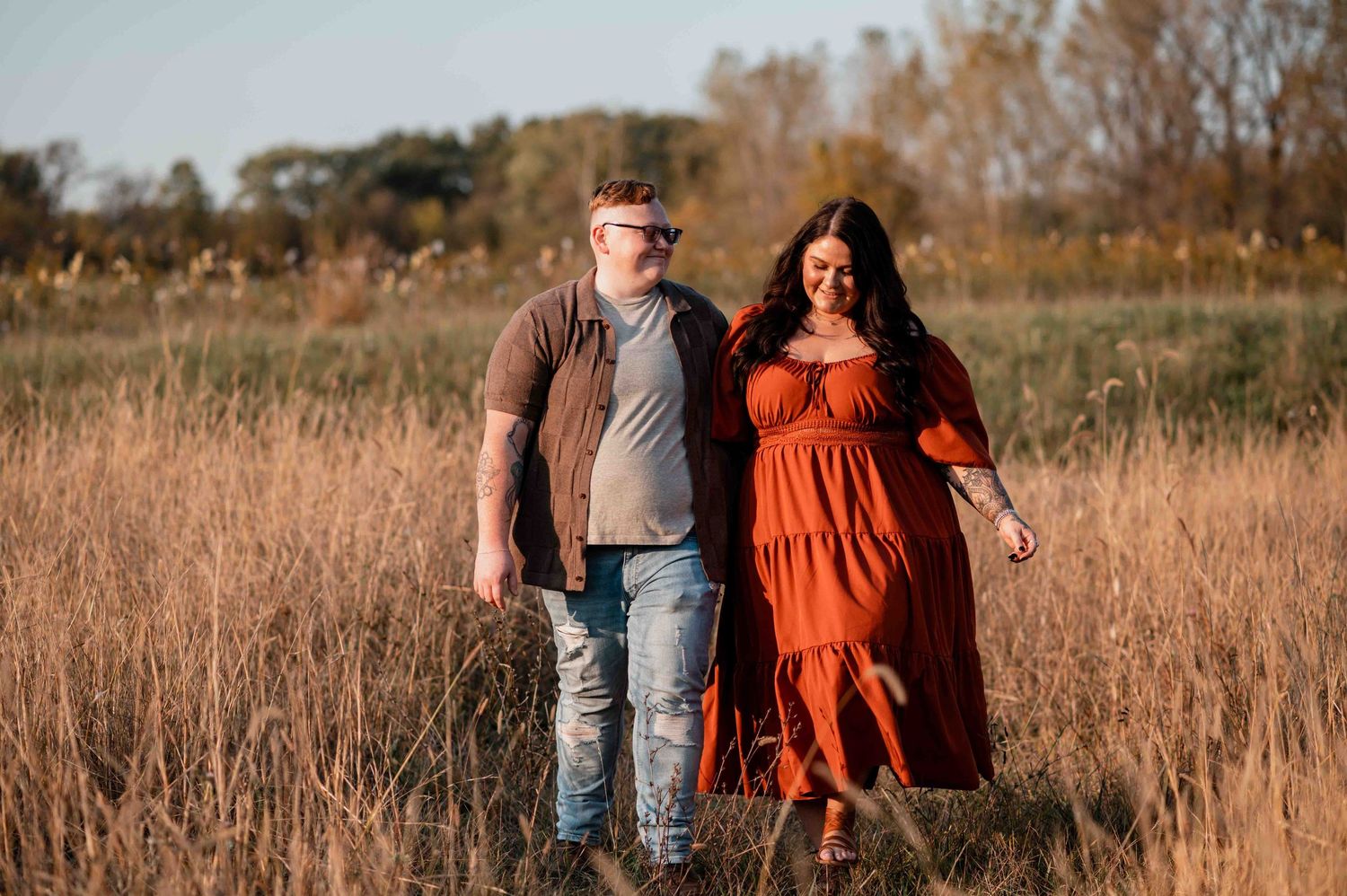 Couple walking through tall autumn grass at golden hour.