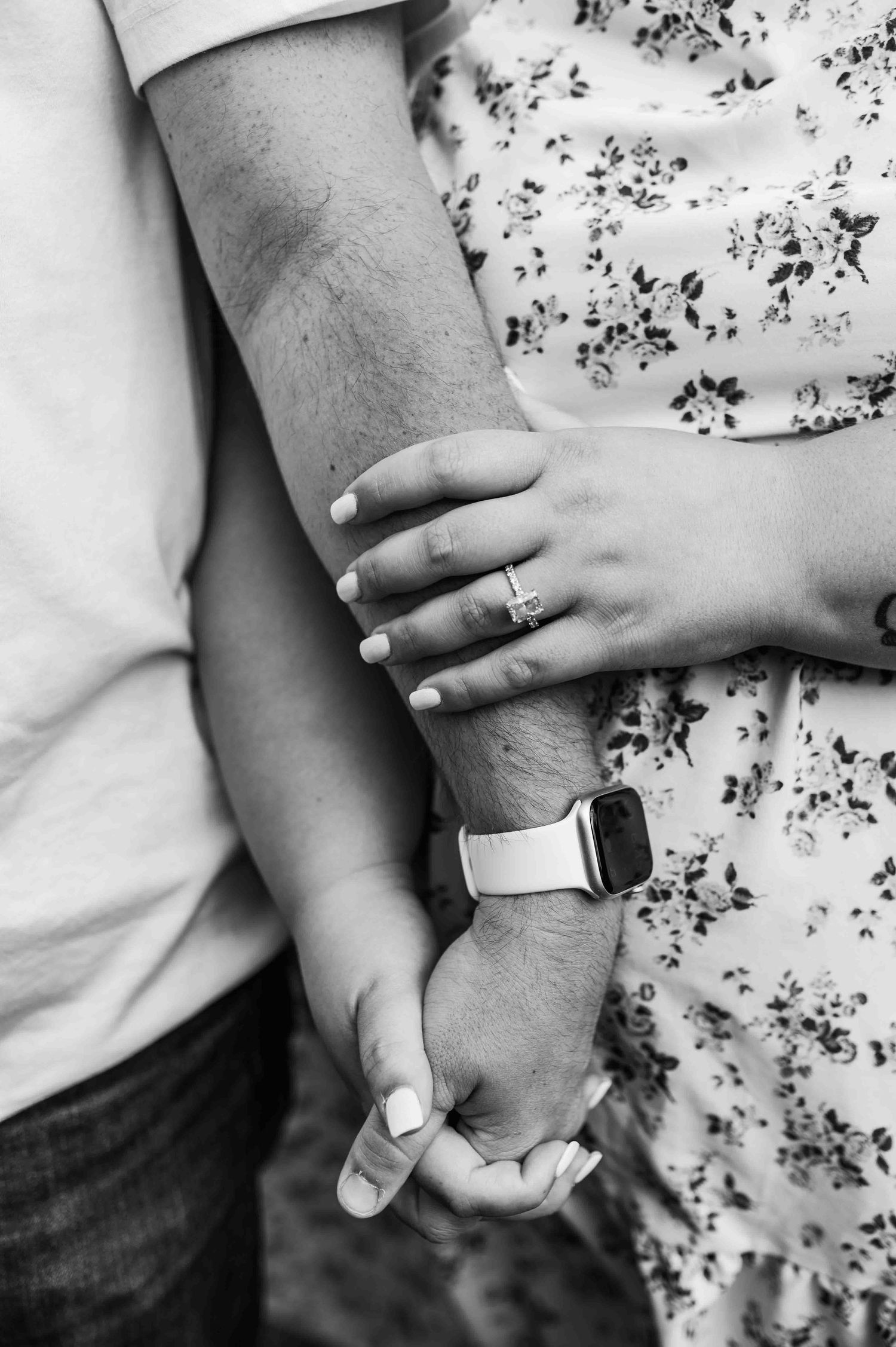 Close-up of intertwined hands with wedding rings against a floral pattern dress.