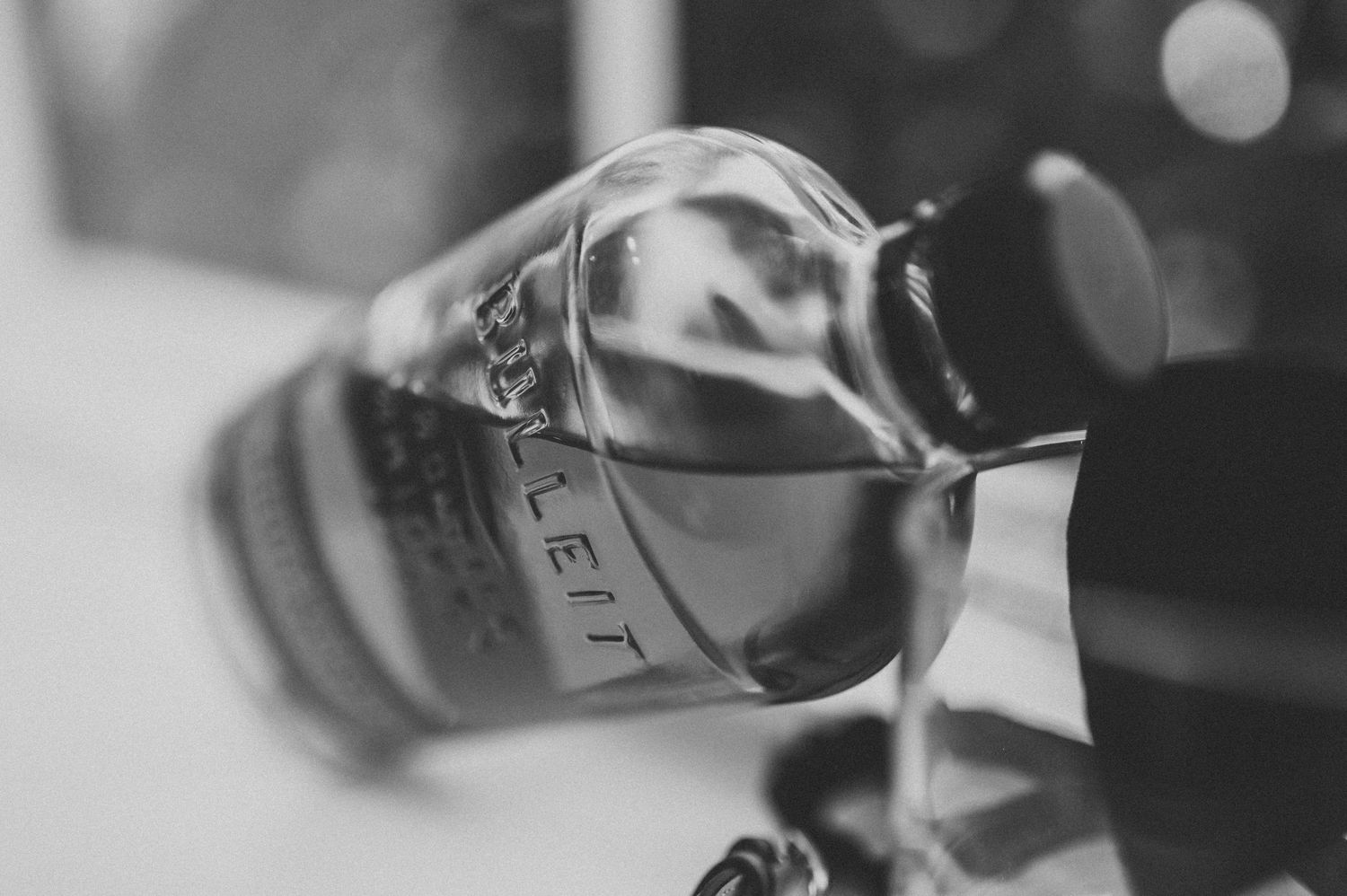 Black and white close-up of whiskey being poured from an elegant bottle, capturing the liquid stream in motion.