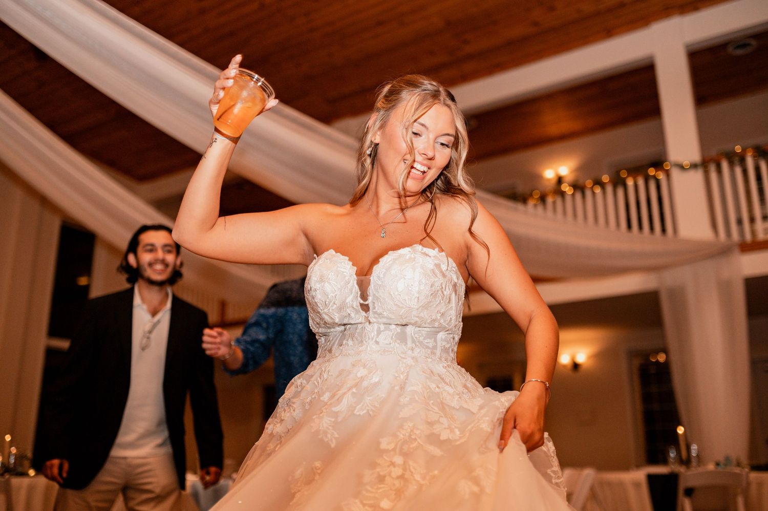 Bride dancing with joy under warm reception lighting with arms raised.