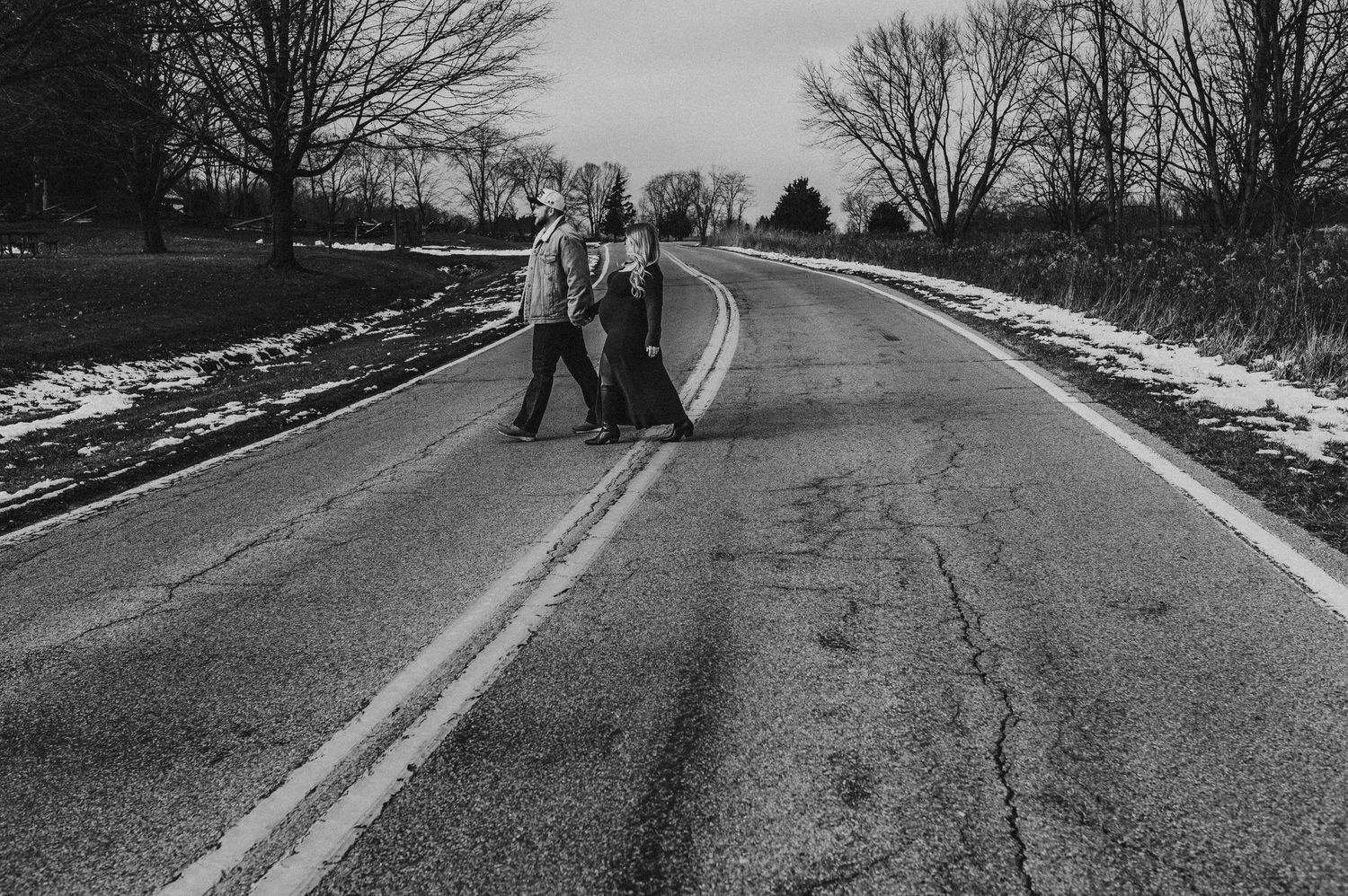 Two people standing on a rural road in winter, black and white photography with snow on the sides.