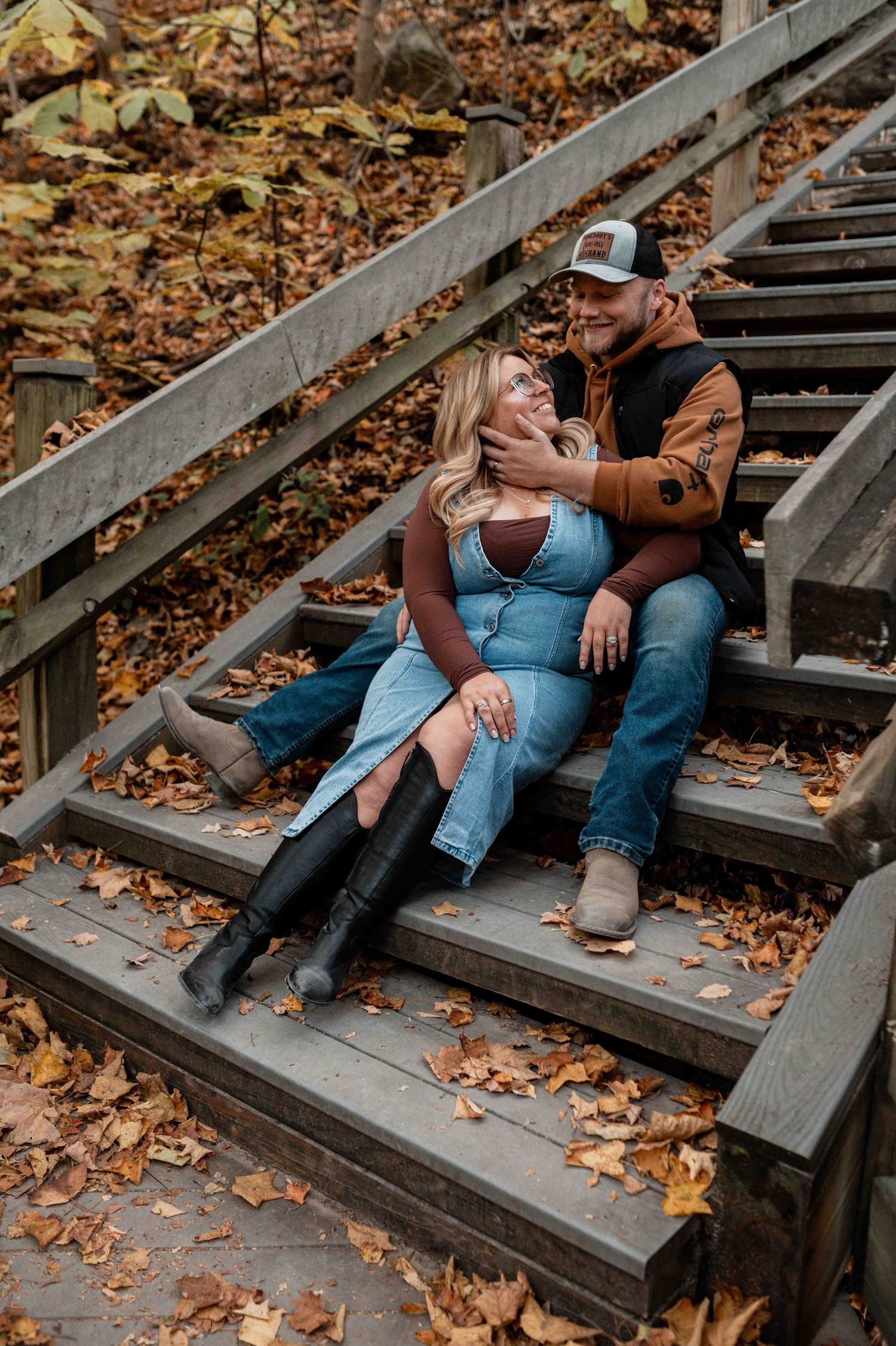 Couple relaxing on wooden steps covered in autumn leaves during outdoor photoshoot.