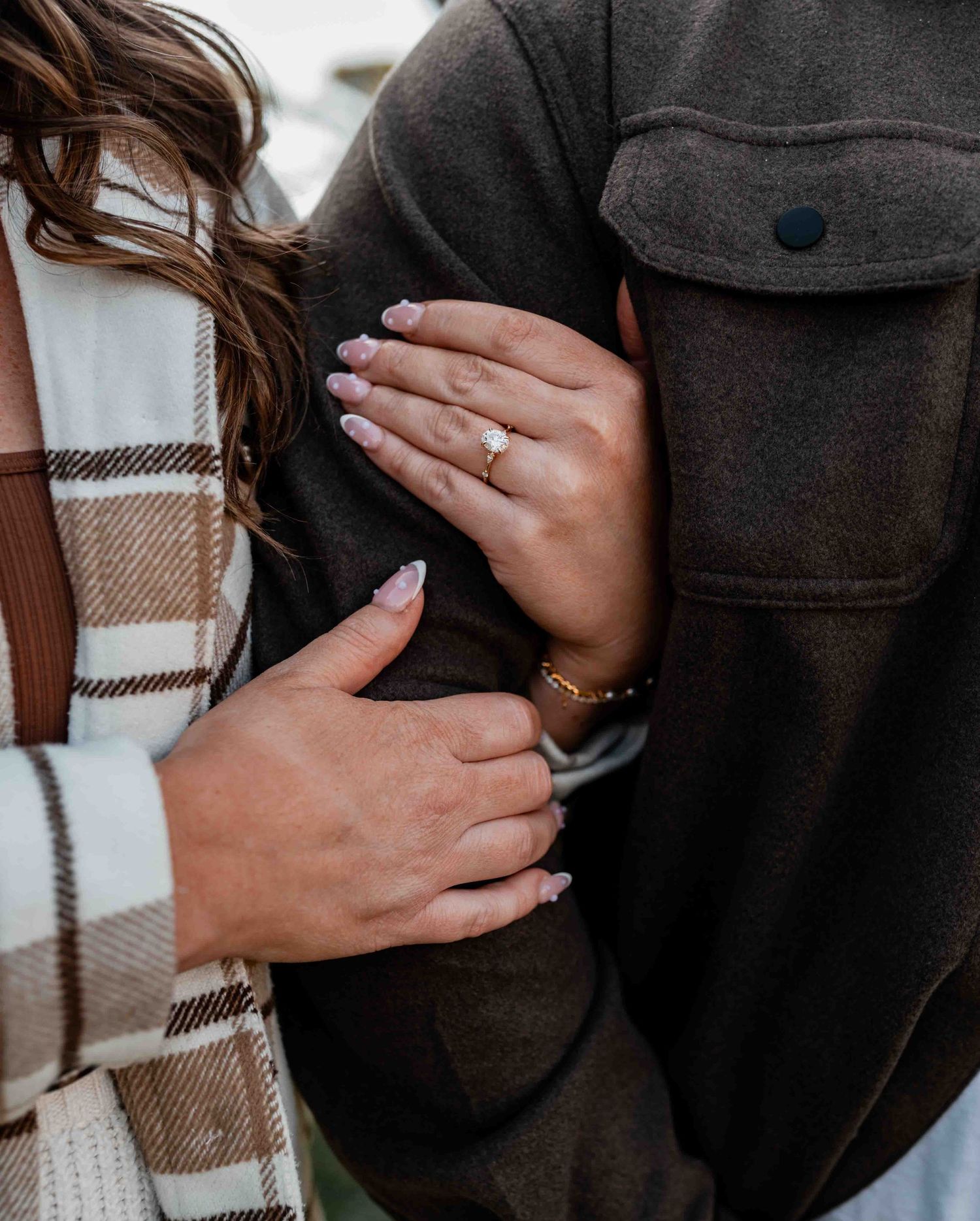 Close-up of hands wearing rings against a plaid blanket background.