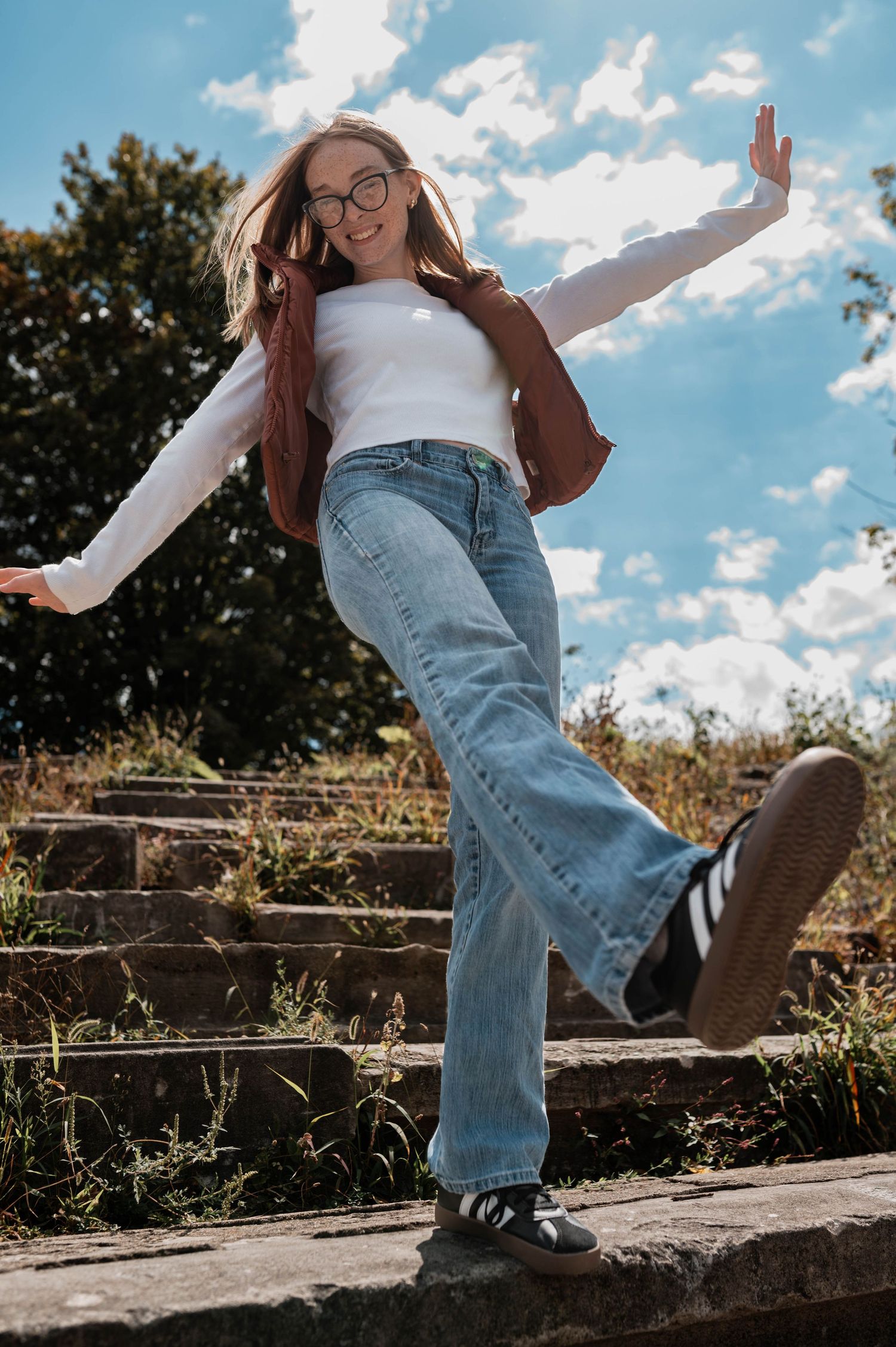 Person in jeans and white top lounging on wooden fence against blue sky.