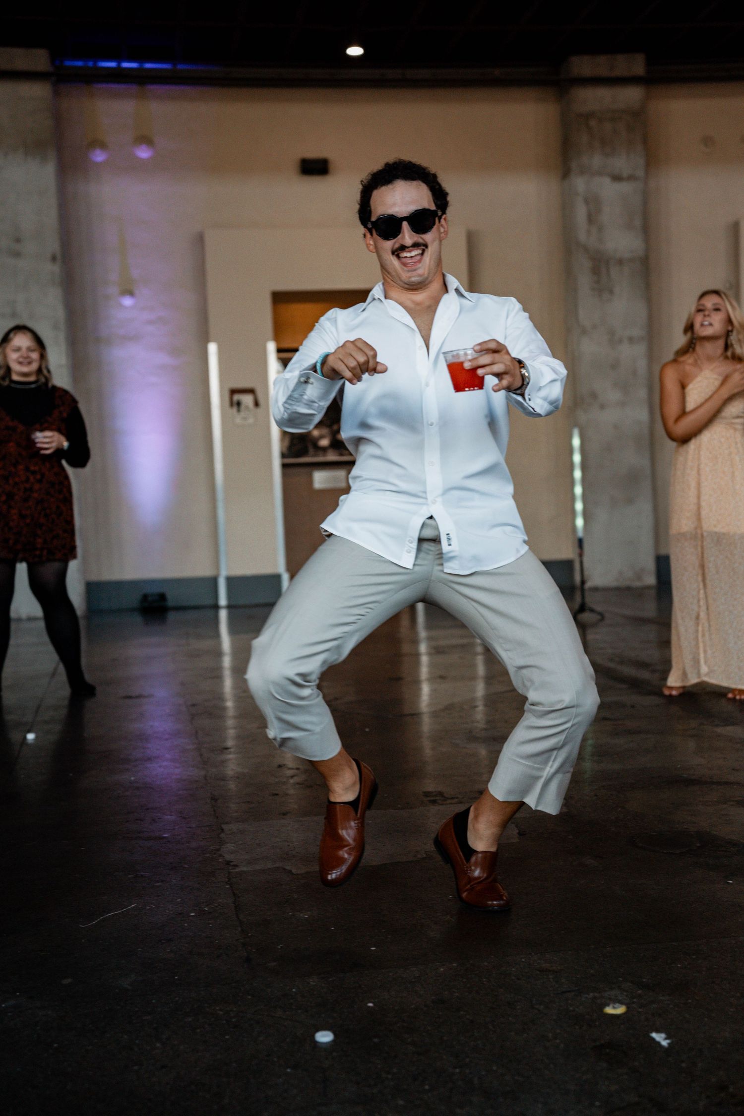 Person in white outfit dancing energetically on dark floor with purple lighting.