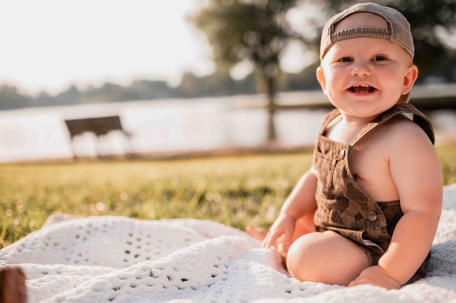 Baby wearing baseball cap lying on blanket outdoors during summer photoshoot.