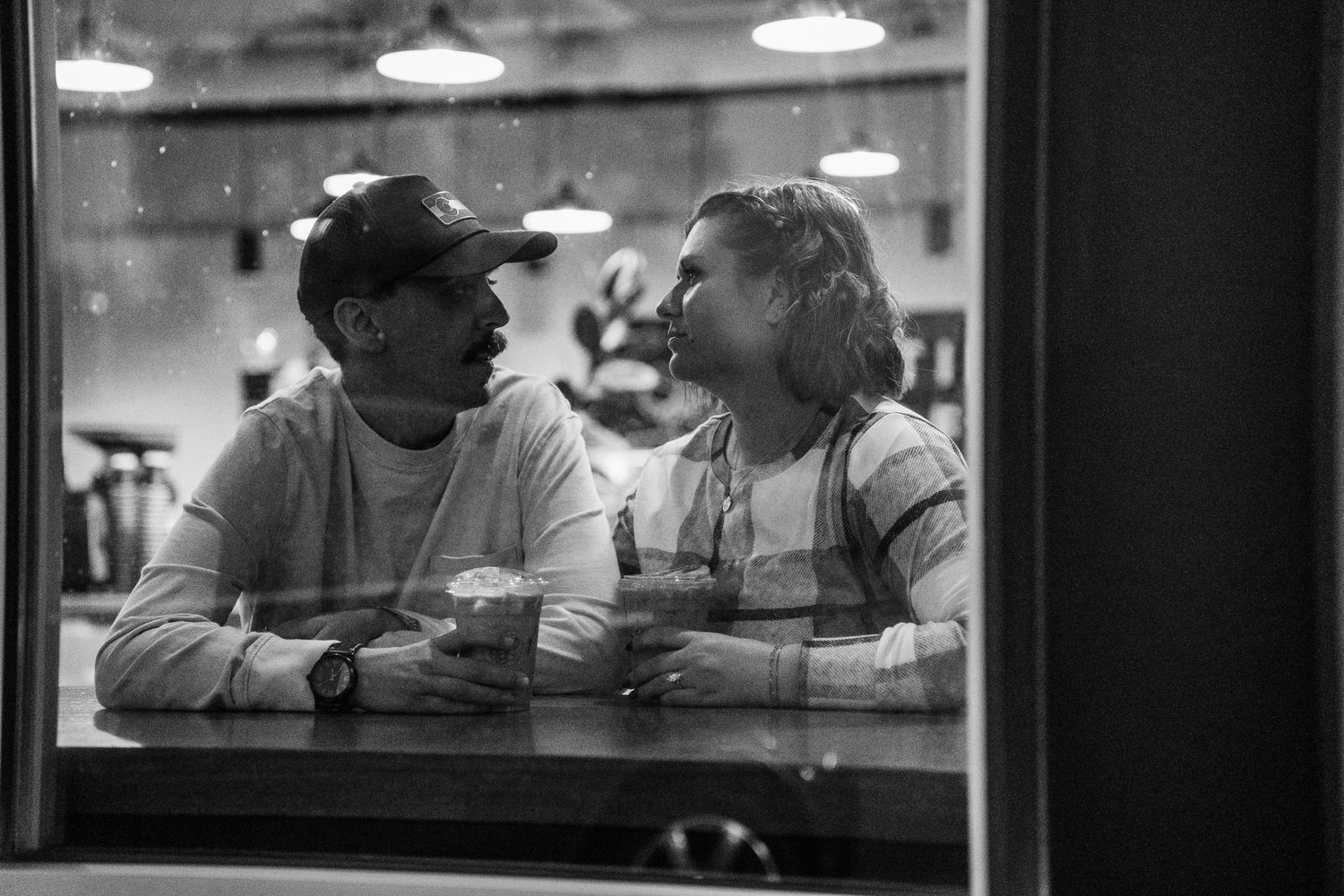 Black and white photo of a couple sharing a romantic moment at a cafe table, smiling at each other.