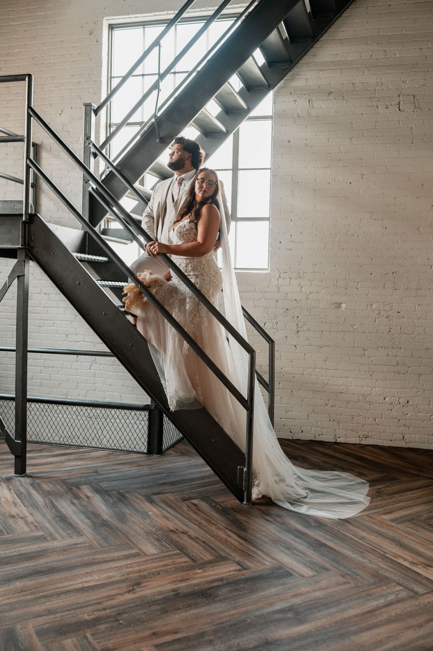 Wedding photography session featuring industrial staircase and white gown against brick wall.