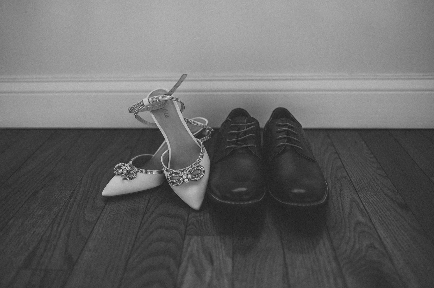 Wedding shoes lined up on dark hardwood floor against white baseboards.