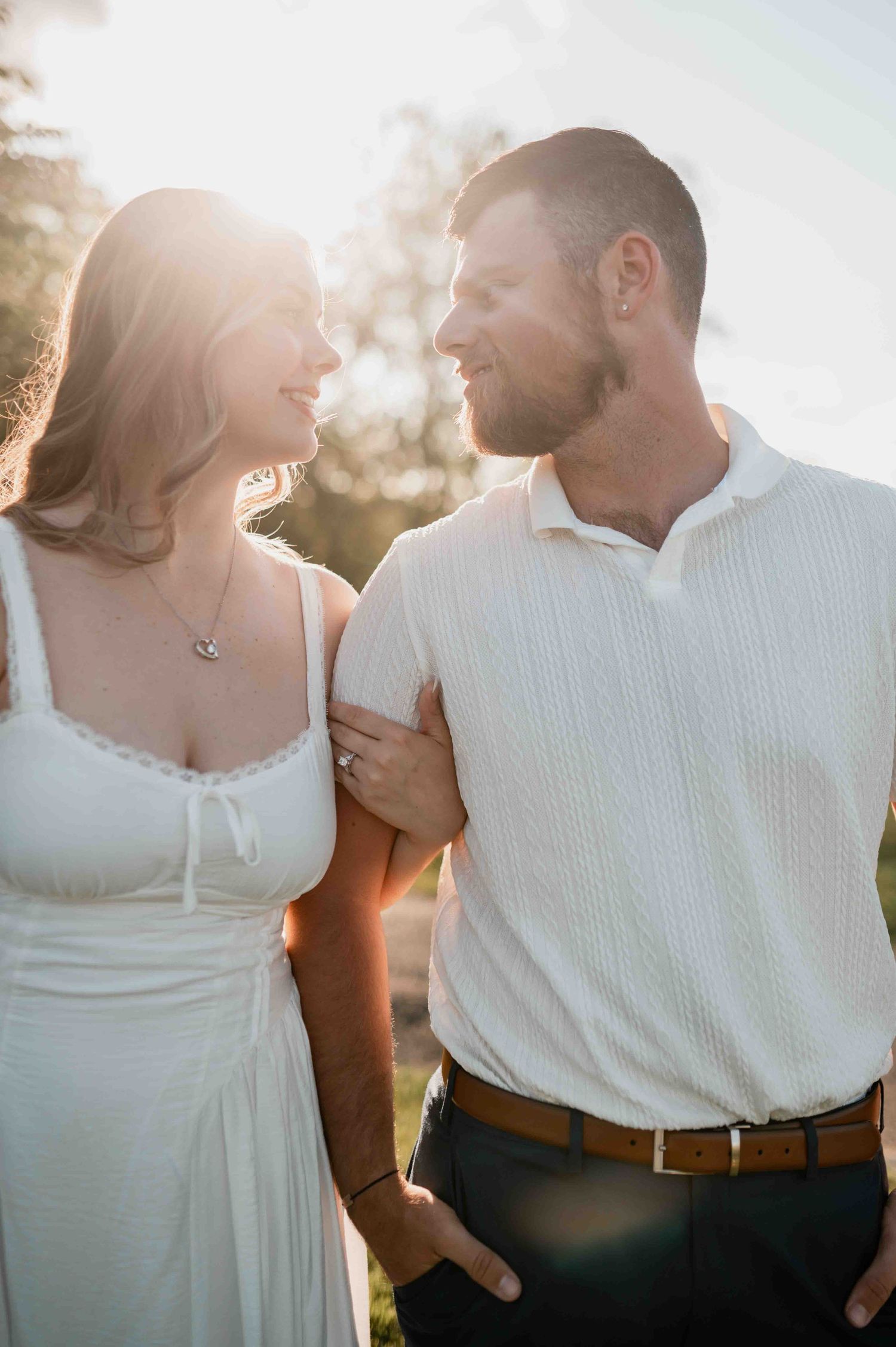 Sunlit portrait of couple in white clothing sharing intimate moment outdoors.