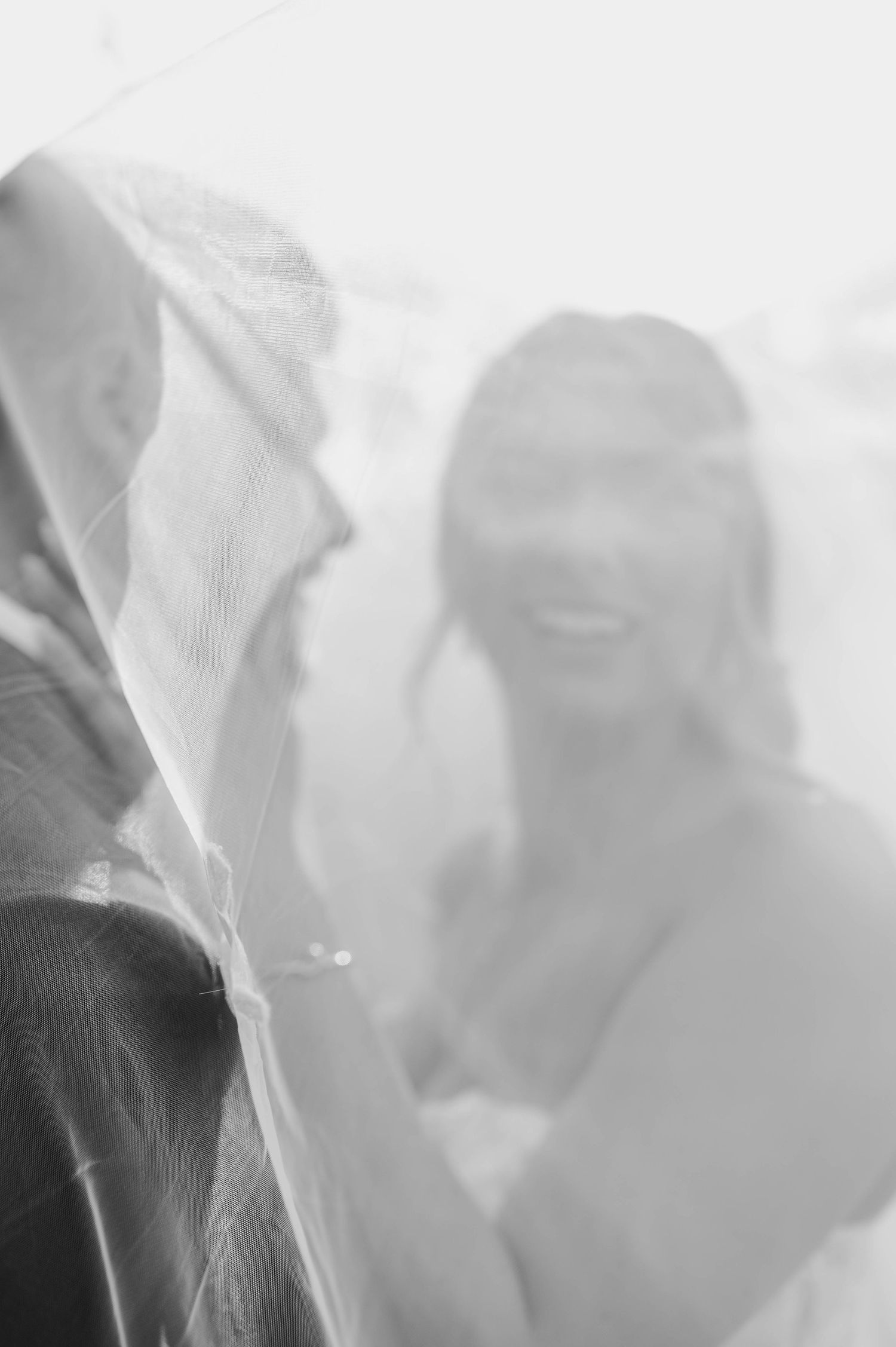 Soft ethereal bridal portraits through white veil create dreamy wedding day atmosphere.