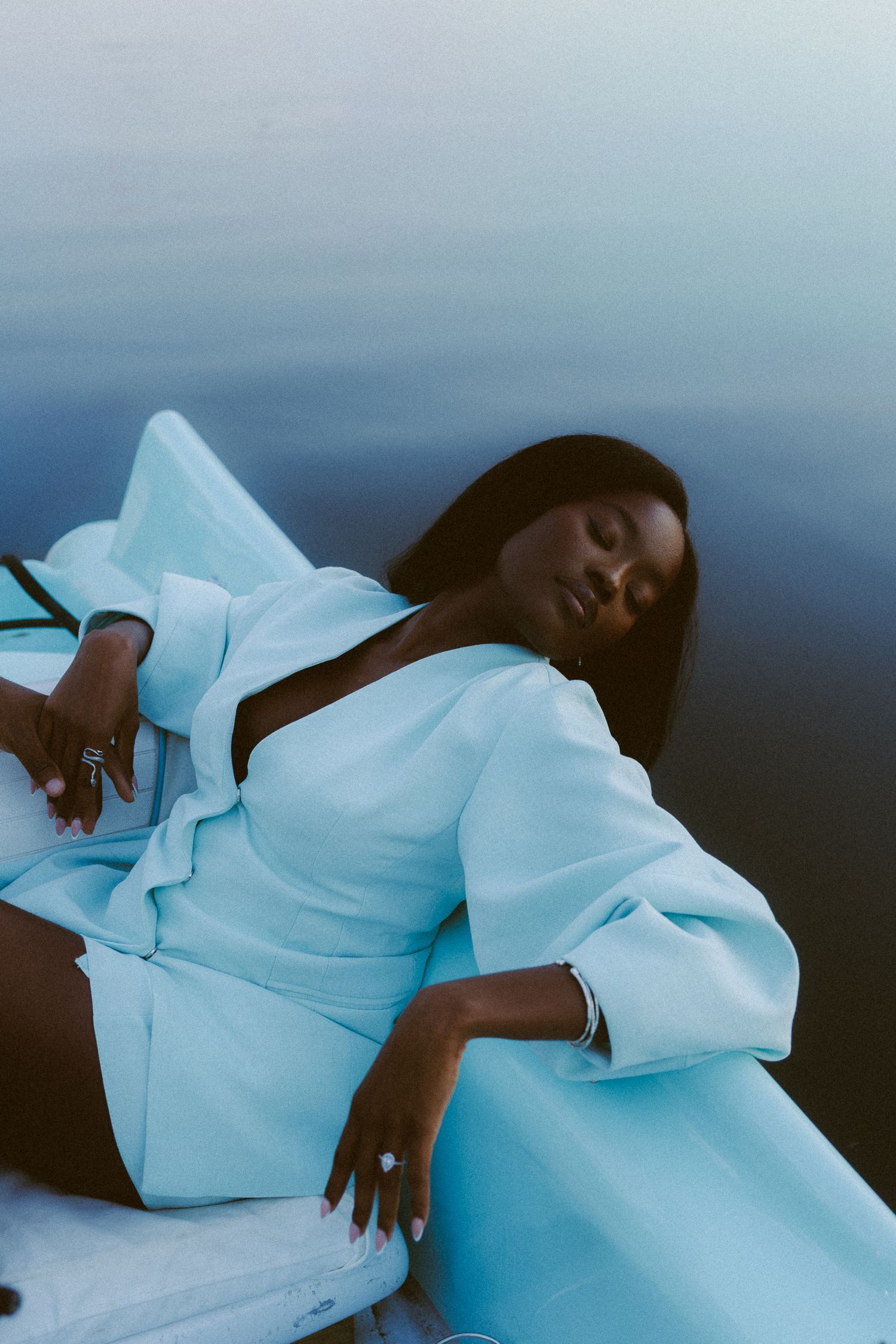 A person in a flowing light blue dress rests peacefully against a dark moody background.