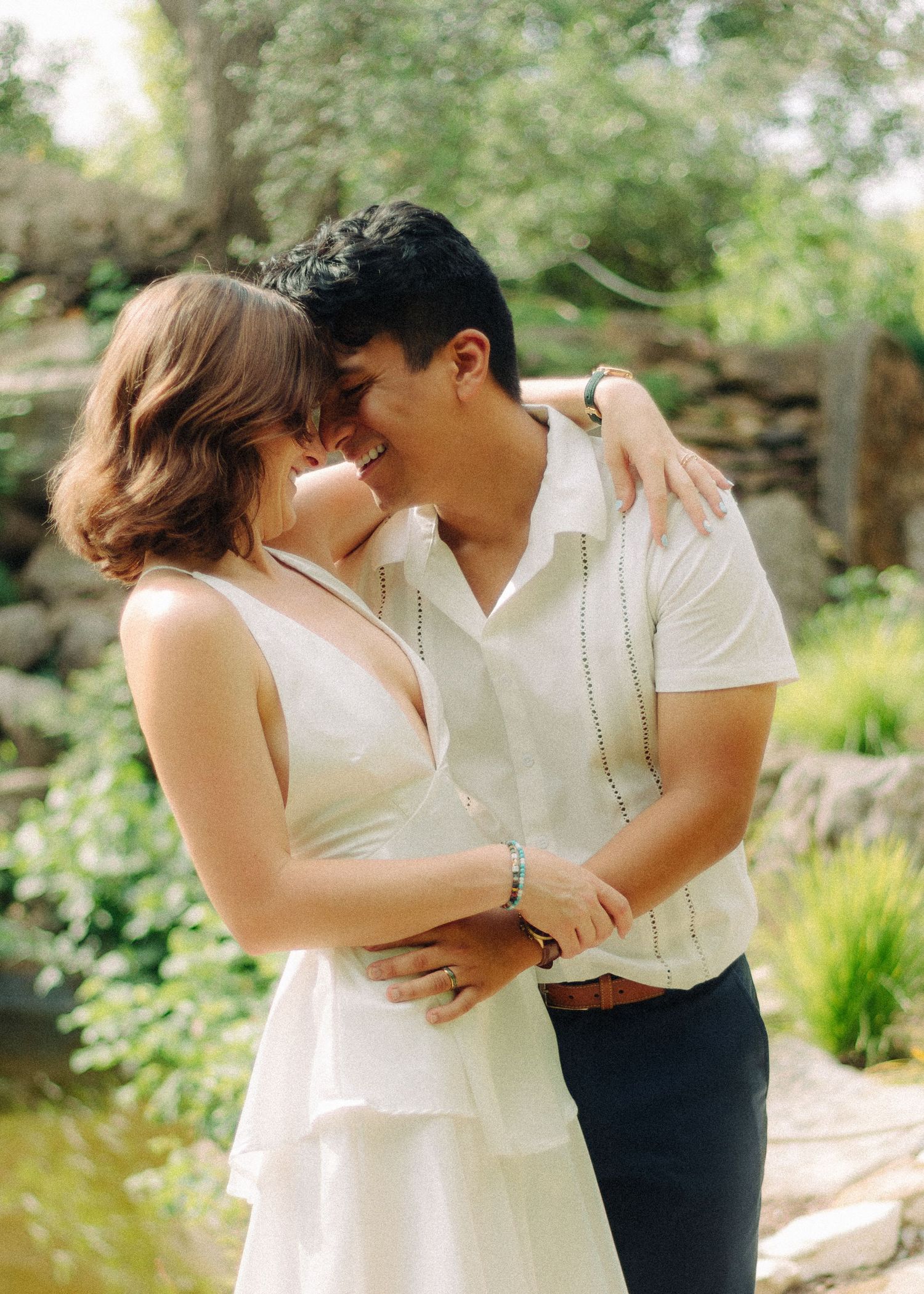 Romantic moment captured between couple in white outfits against green garden backdrop.