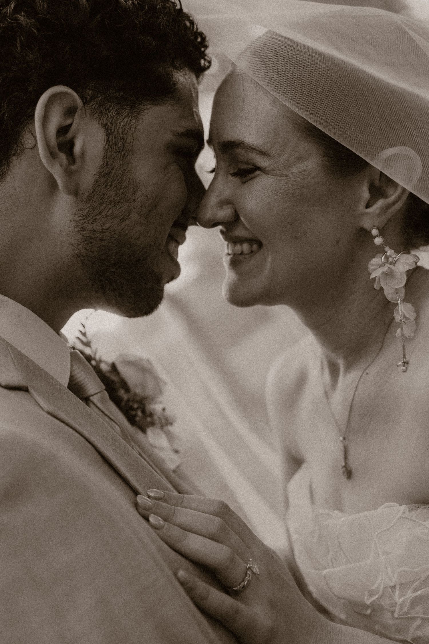 Black and white photo of a smiling bride and groom touching foreheads on their wedding day.
