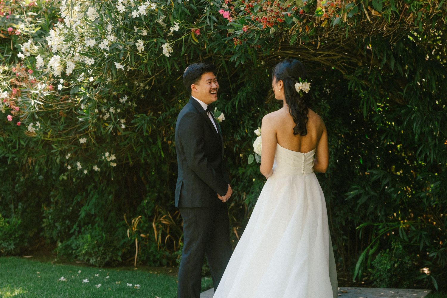 Bride and groom share a romantic first look moment in a lush garden with blooming flowers.