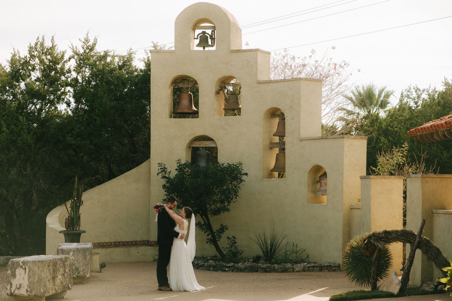 A Spanish colonial style wedding chapel with white stucco walls and bell tower stands against a desert landscape.