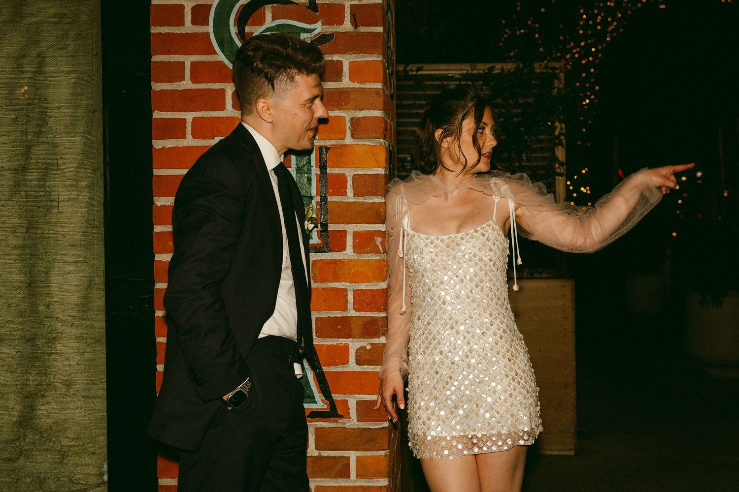 Couple in formal attire celebrate outdoors, bride wearing a sparkling sequined mini dress at night.
