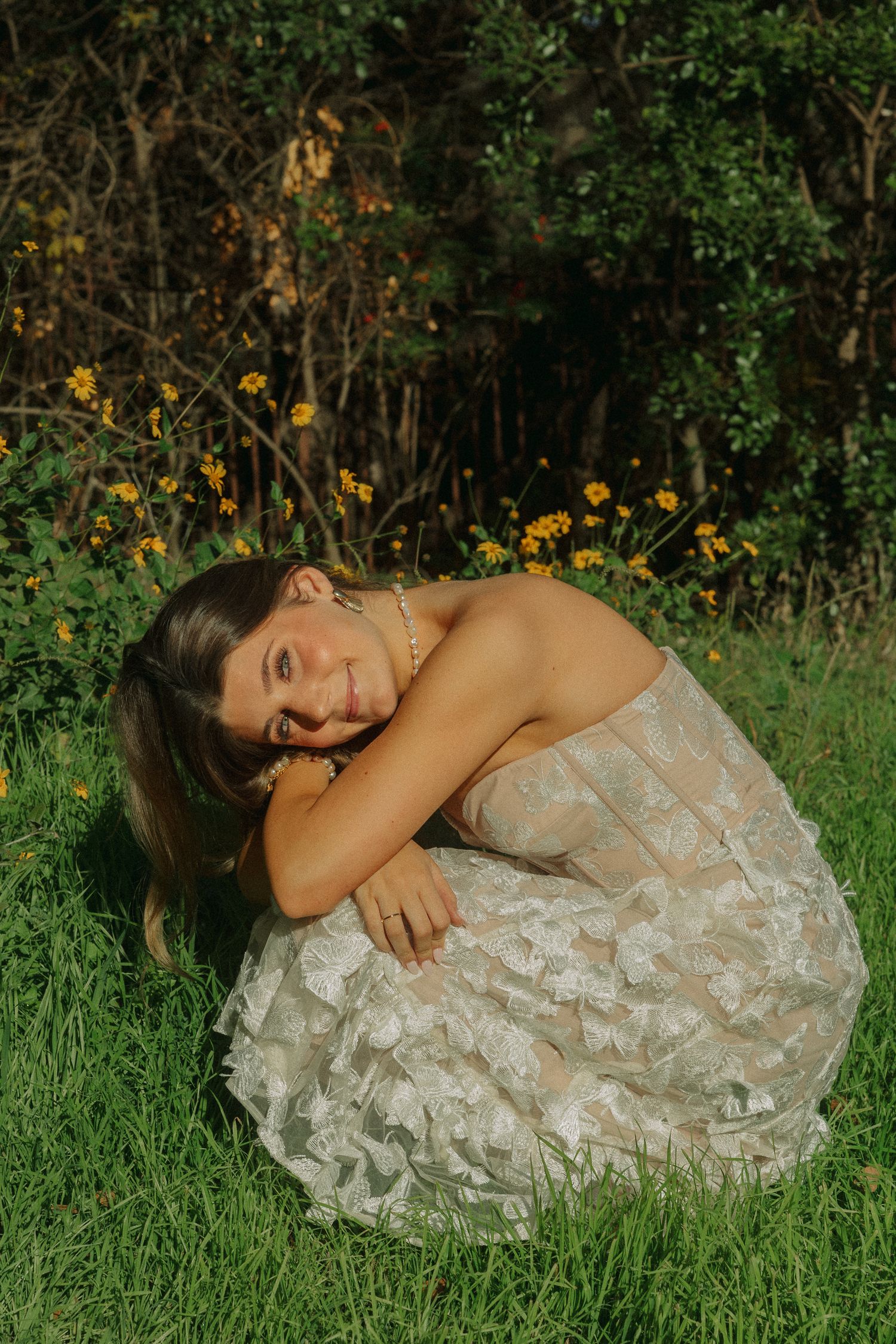 A white lace dress flows elegantly across green grass in an outdoor garden setting.