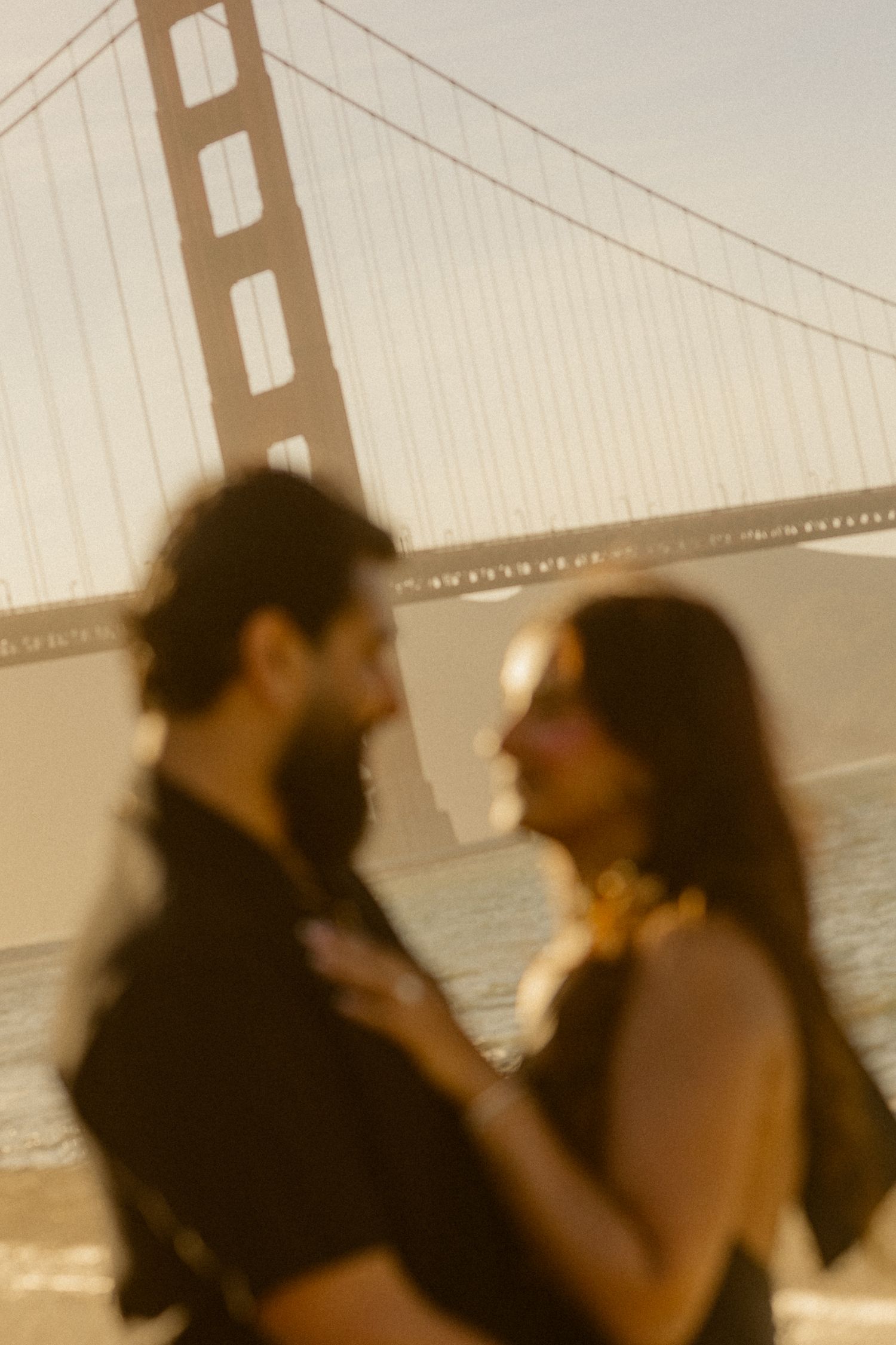 Couple sharing a romantic moment on the beach with the Golden Gate Bridge glowing in the warm sunset light.