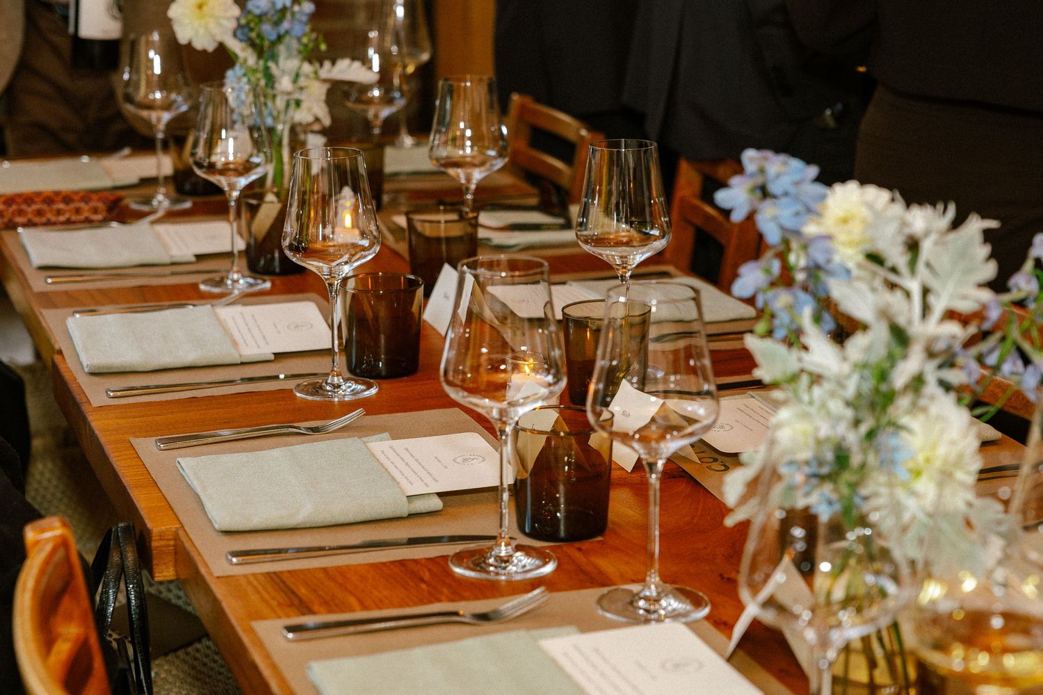 Elegant dining table set with crystal wine glasses, candles, linen napkins, and fresh blue floral arrangements for a formal dinner.