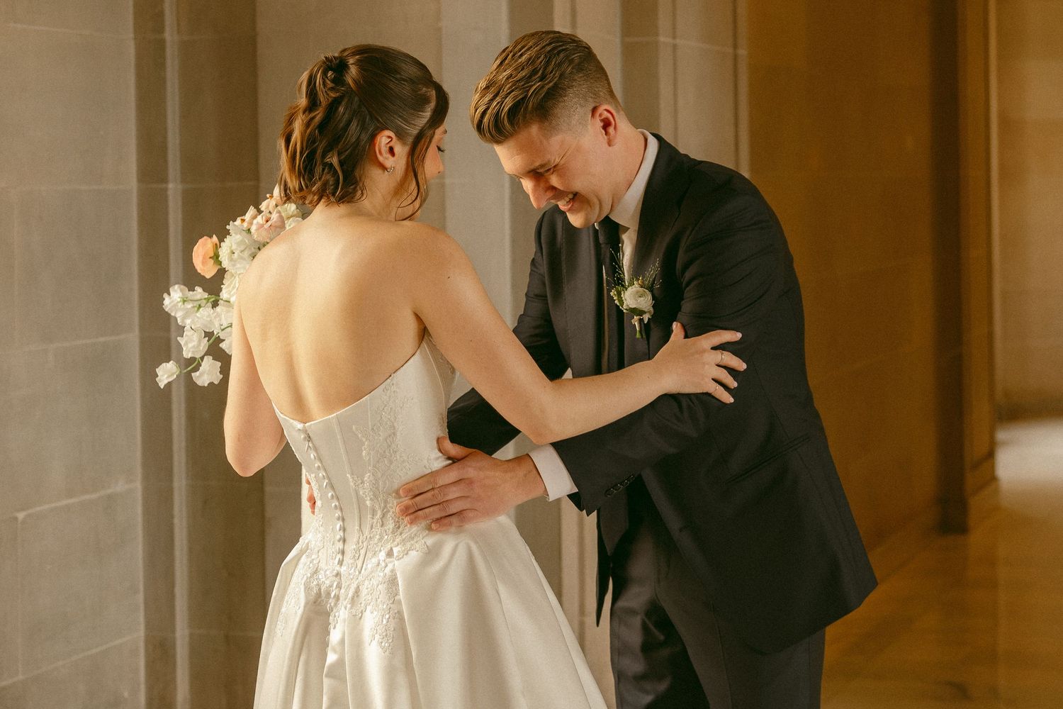 Bride in strapless white corset gown holding bouquet faces groom in black suit during intimate wedding moment.