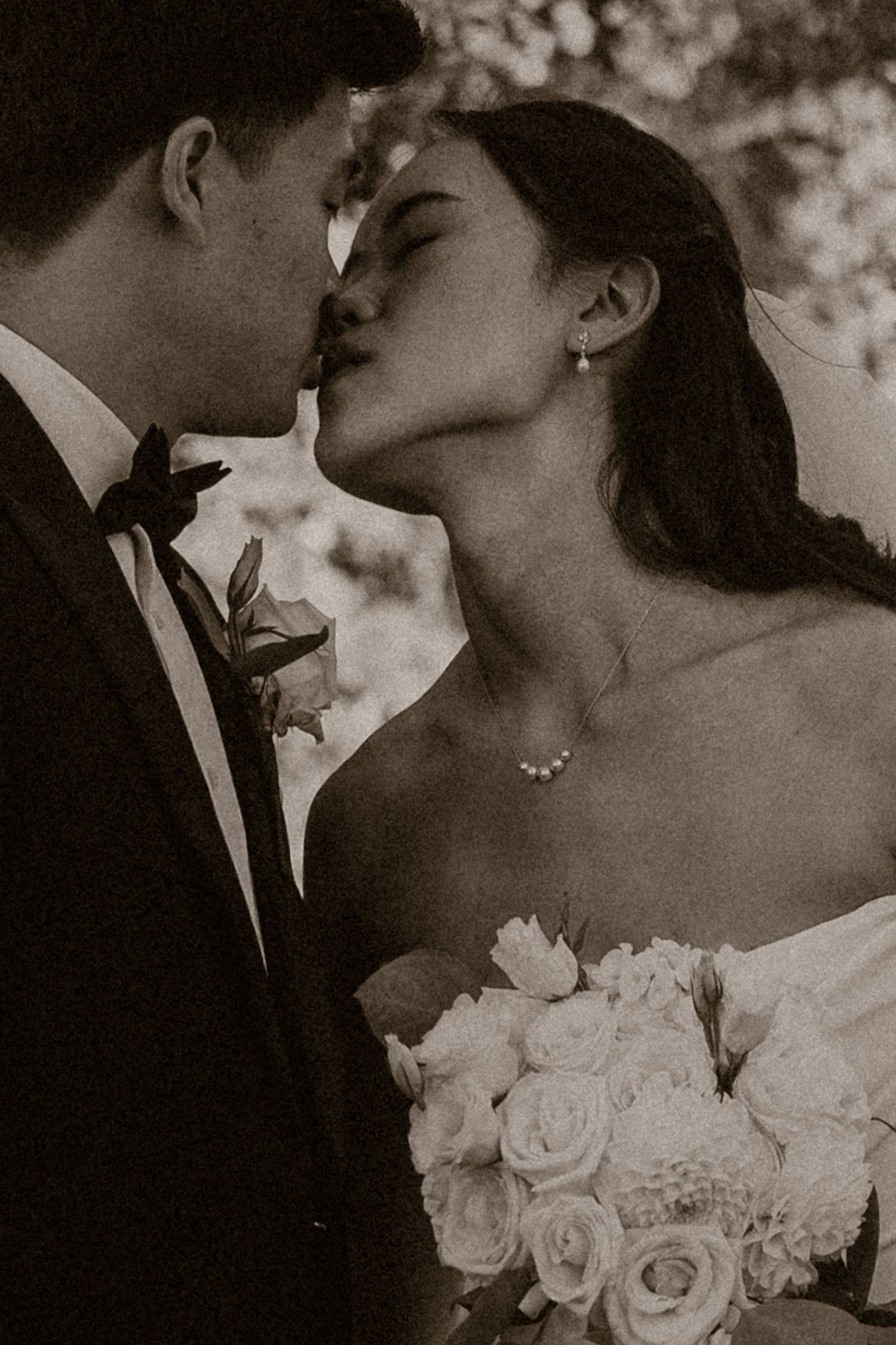 Black and white photo of a bride and groom sharing a romantic kiss, bride holding white rose bouquet.