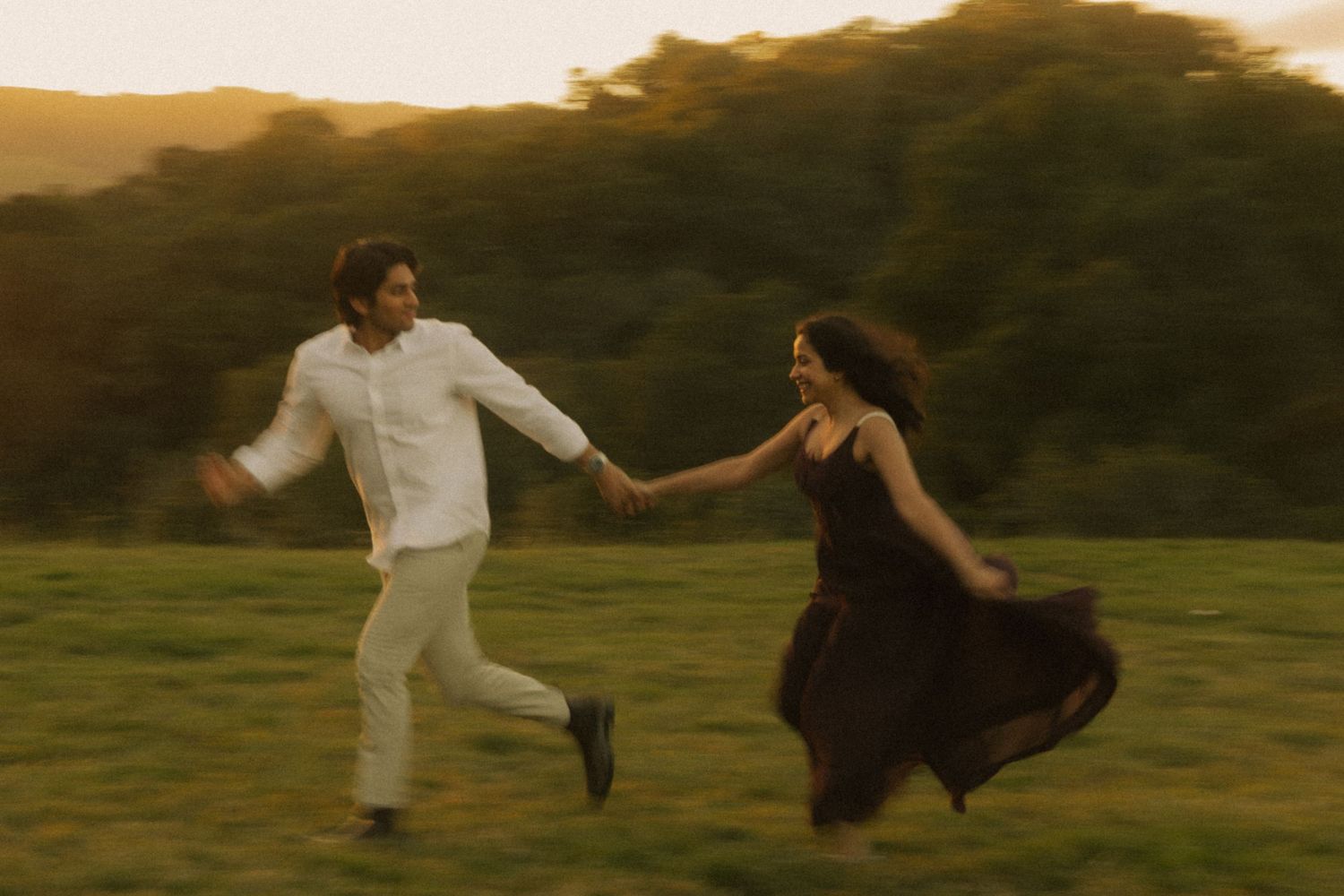 Couple running and dancing playfully in a field during golden hour.