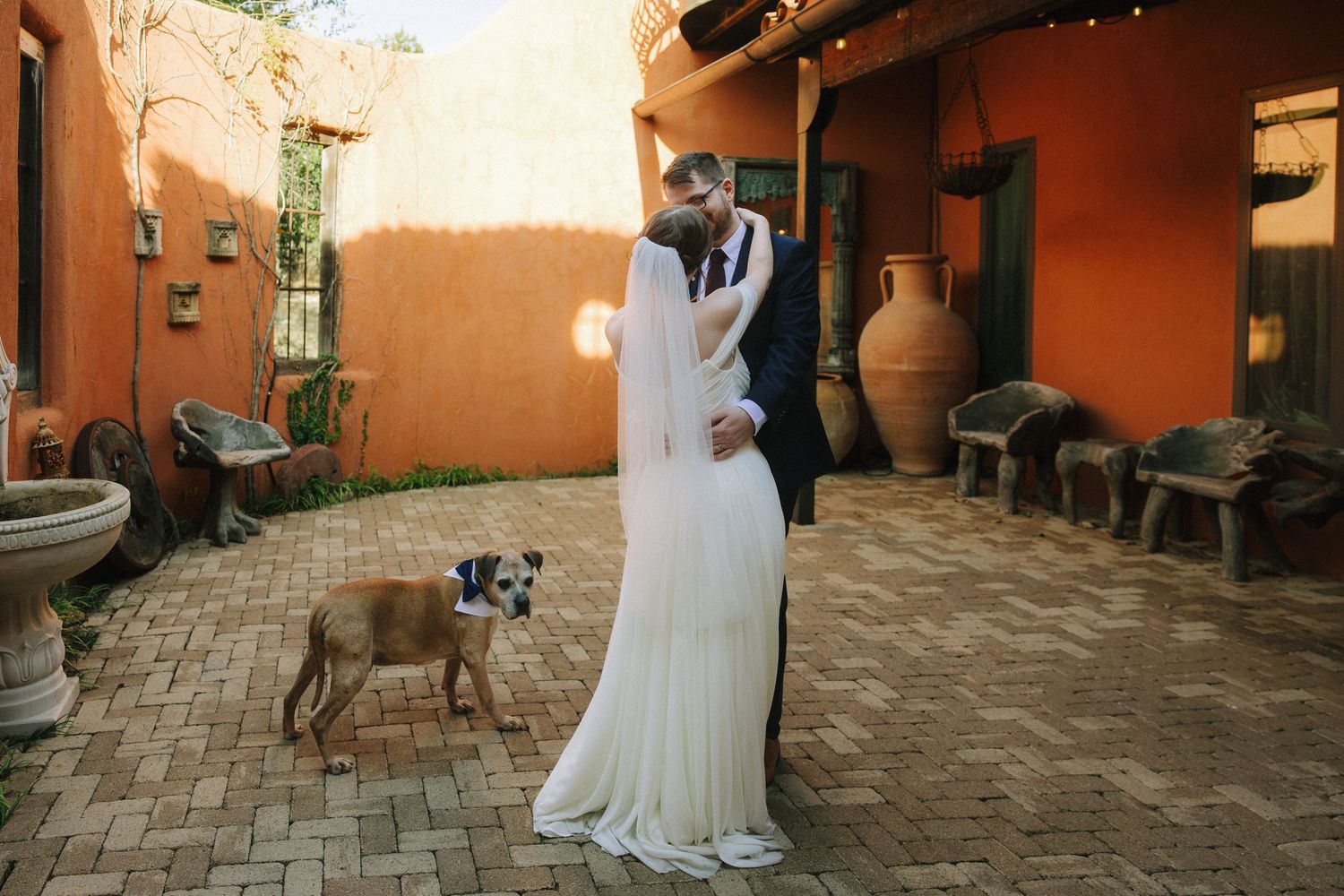 A series of wedding photos showing a couple and their dog in a rustic outdoor courtyard setting with terracotta walls.
