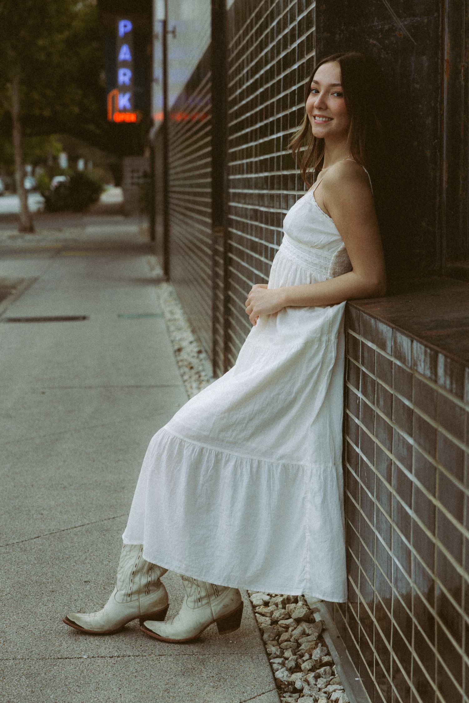 A white summer dress contrasts against an industrial metal fence on a city sidewalk.