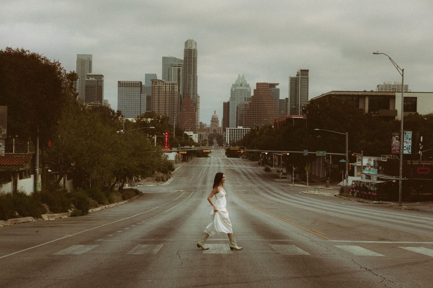 An empty city street with tall buildings and trees during golden hour.