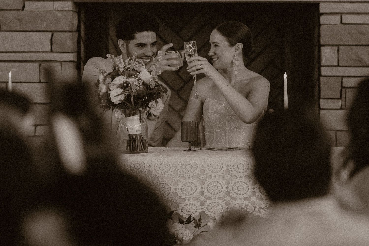Black and white photo of a bride and groom toasting with champagne glasses at their wedding reception.